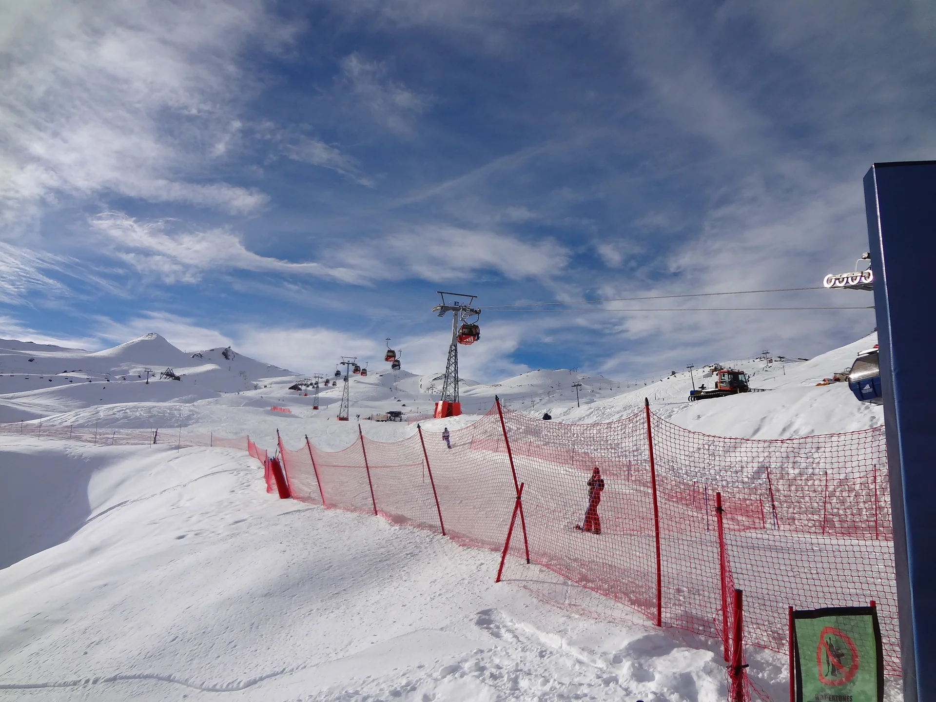 Pista de neve em Valle Nevado com esquiadores distantes, sinalização e montanhas ao fundo.