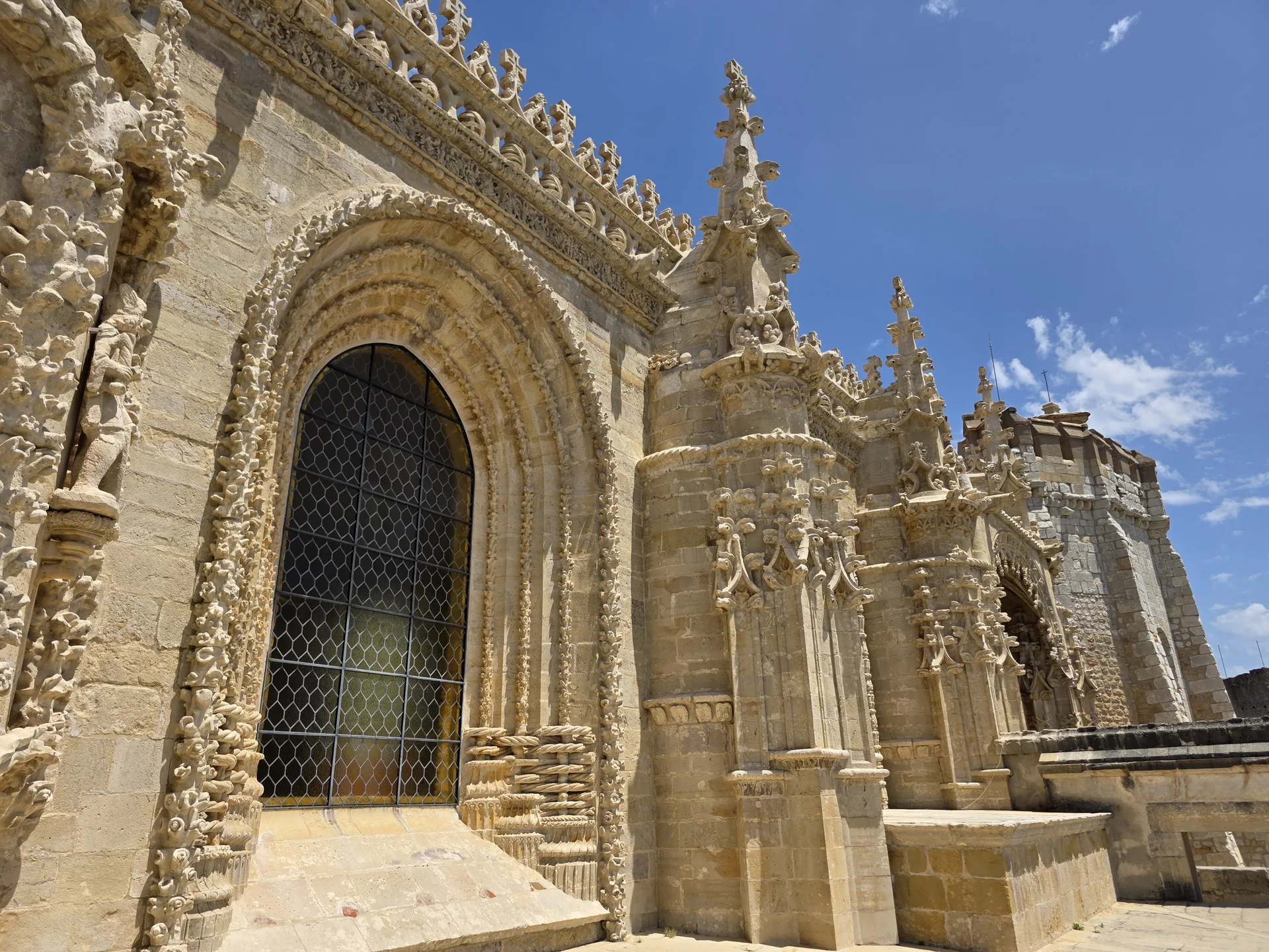 Porta fortificada de pedra e muralhas do Castelo de Tomar sob céu parcialmente nublado.