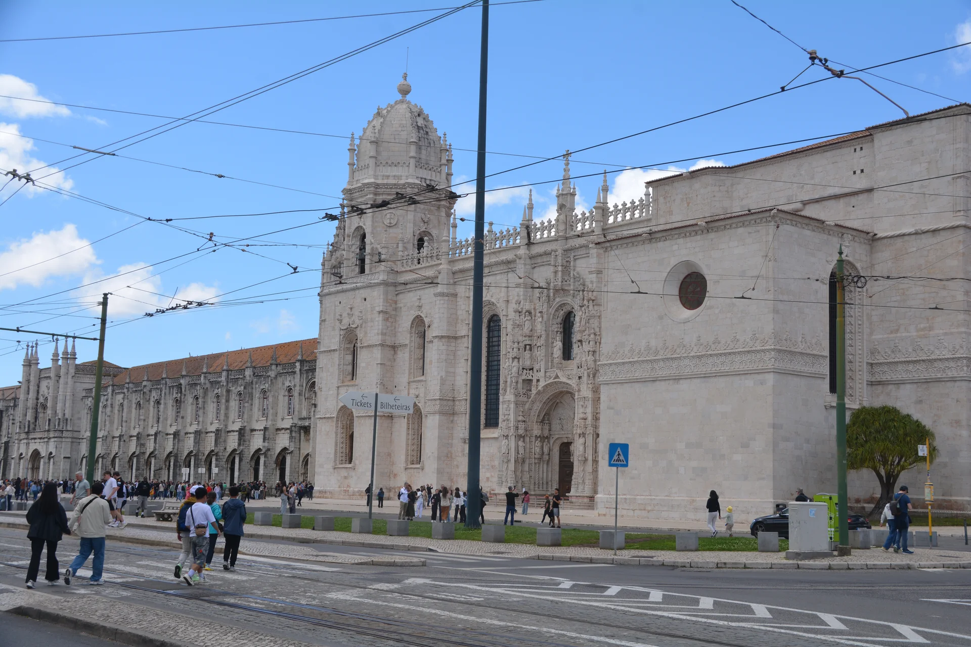 Fachada clara do Mosteiro dos Jerónimos em Belém, Lisboa, vista da rua com trilhos do elétrico e céu azul.