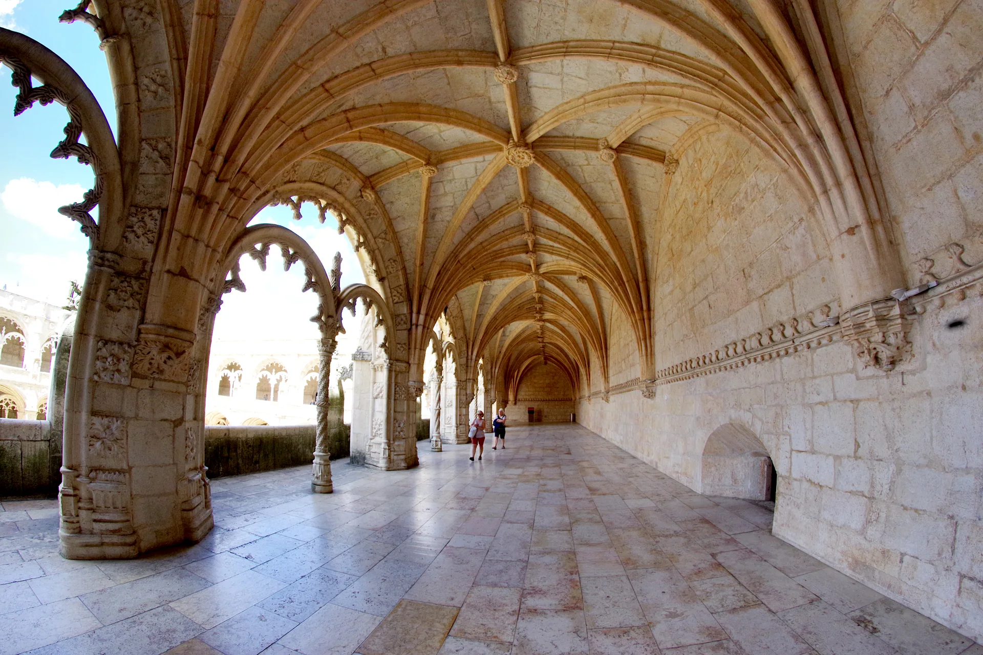 Galeria do claustro do Mosteiro dos Jerónimos com abóbadas nervuradas, arcadas e poucos visitantes em Lisboa.