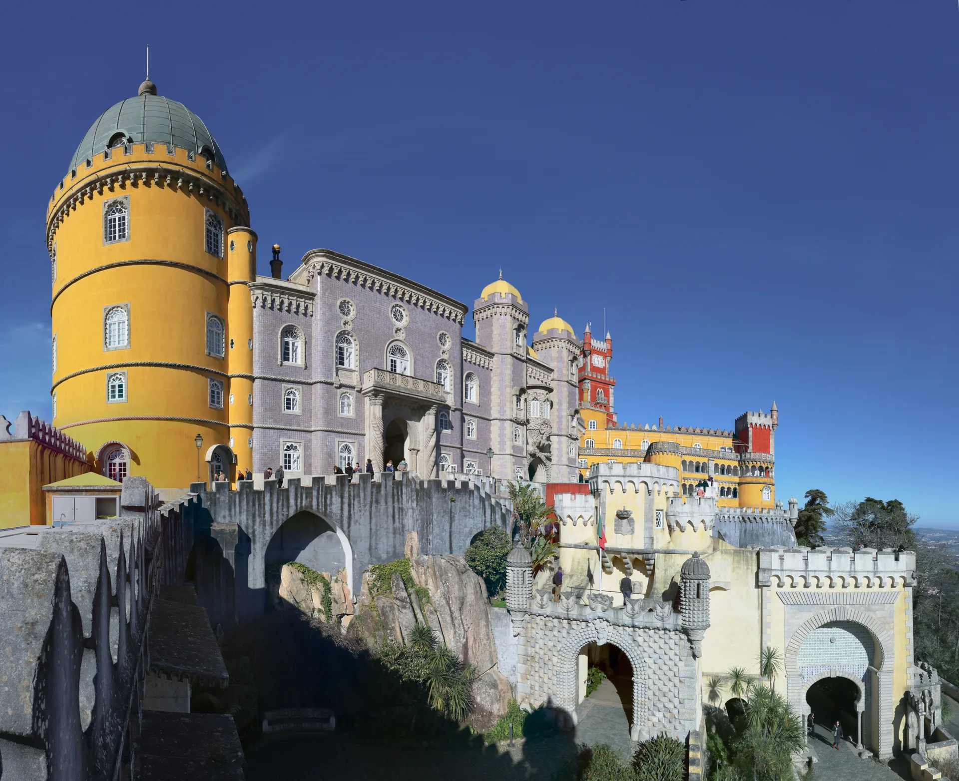 Fachada colorida, muralhas e torres do Palácio Nacional da Pena em dia de céu azul.
