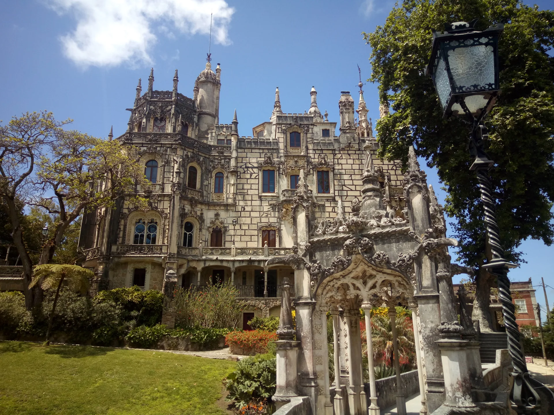 Fachada ornamentada da Quinta da Regaleira entre árvores e vegetação do jardim, em Sintra.