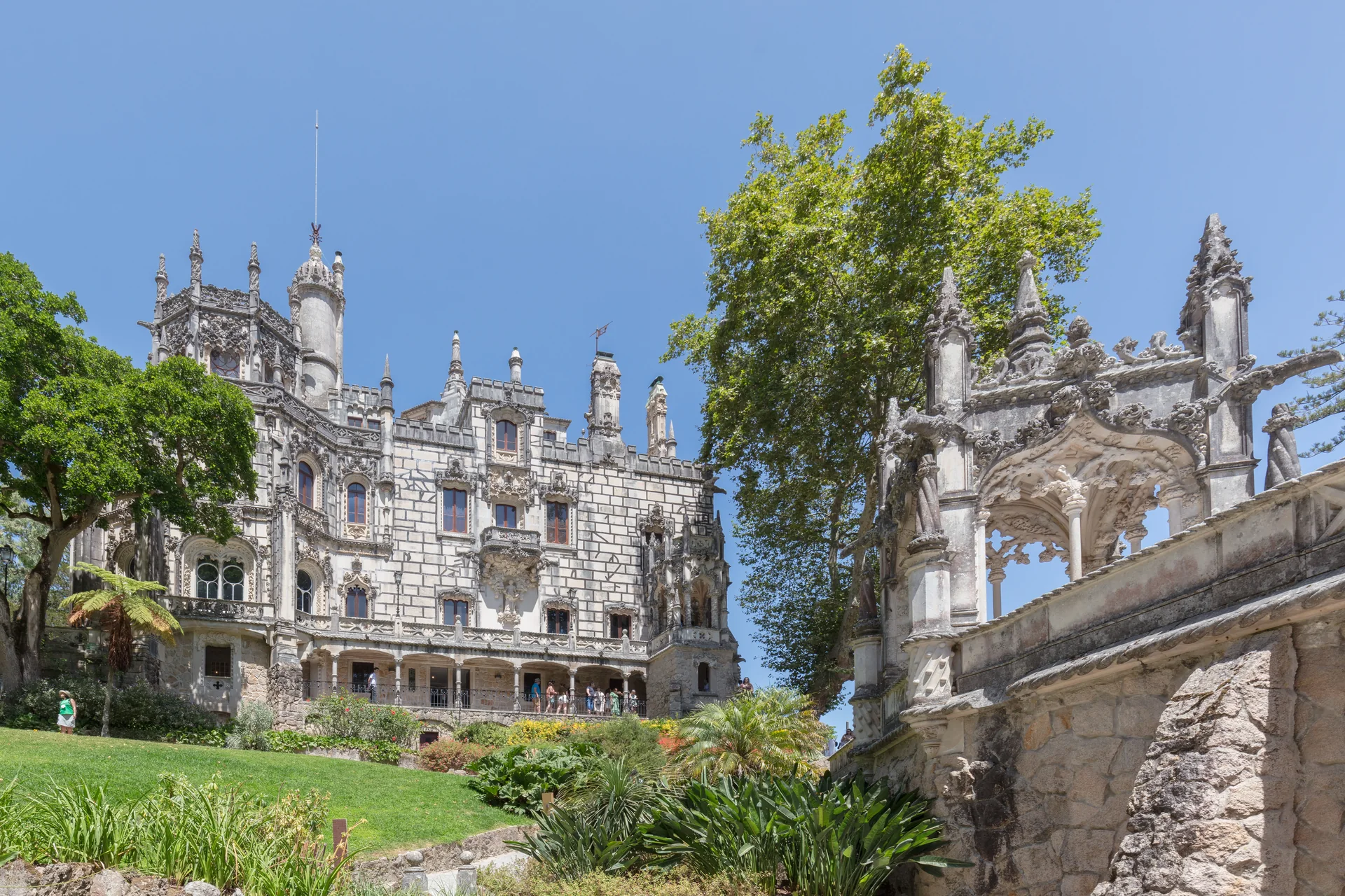 Palácio da Quinta da Regaleira visto a partir do jardim, com gramado, árvores e fachada ornamentada em Sintra.