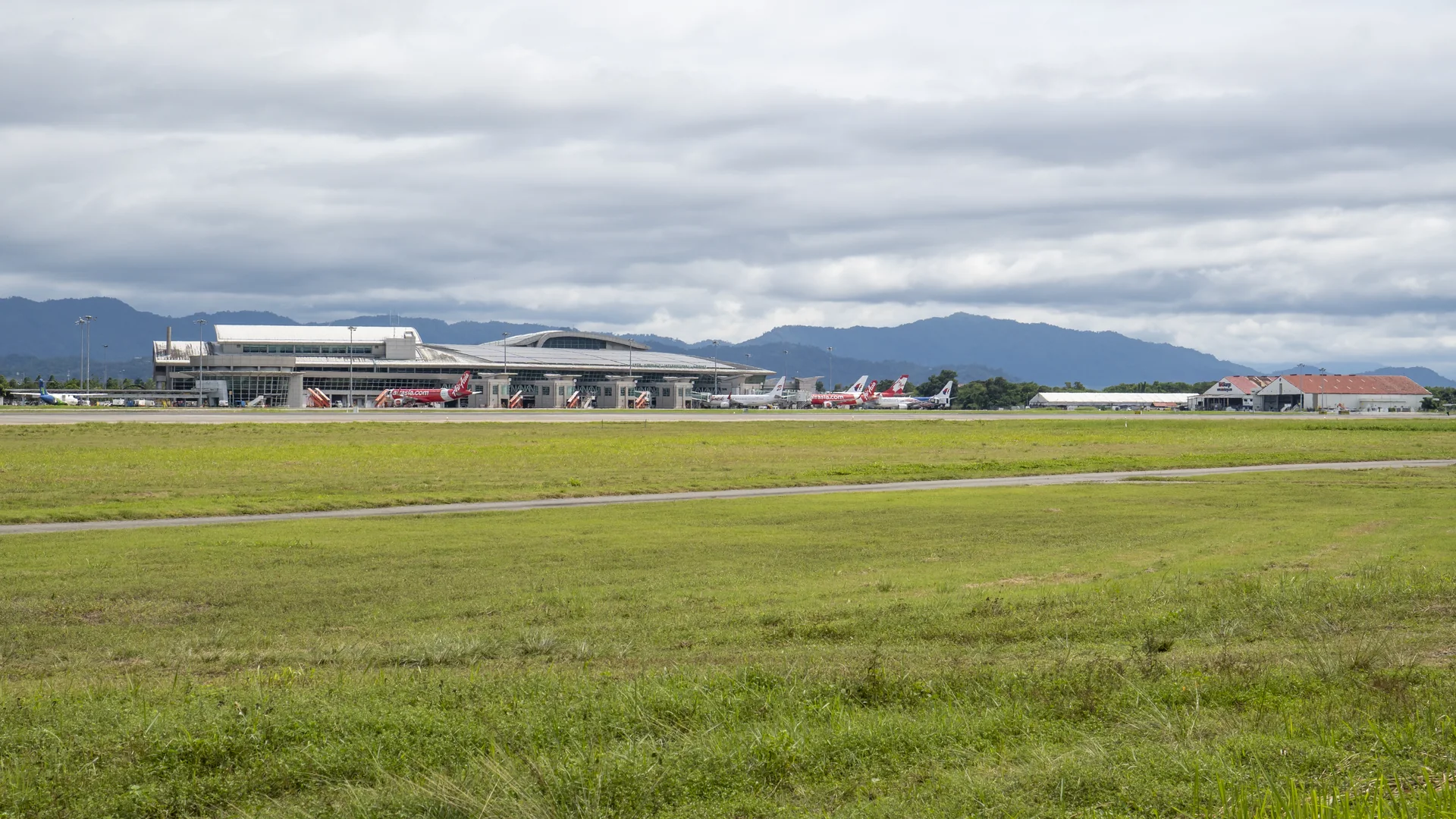 Terminal 1 do Aeroporto Internacional de Kota Kinabalu com aviões em solo e montanhas ao fundo.