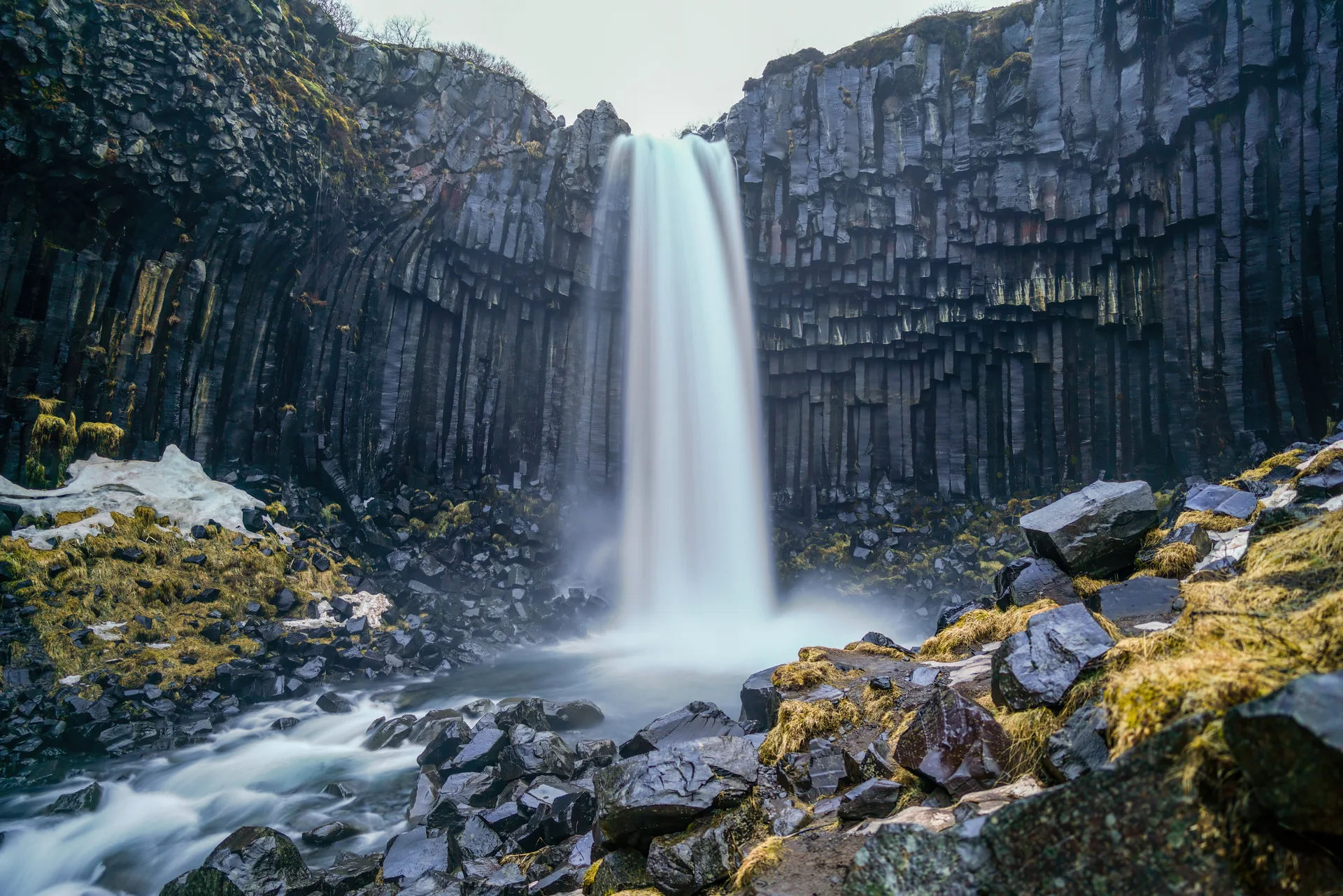 Cachoeira Svartifoss cai diante de colunas de basalto escuro, com rochas e vegetação na Islândia.