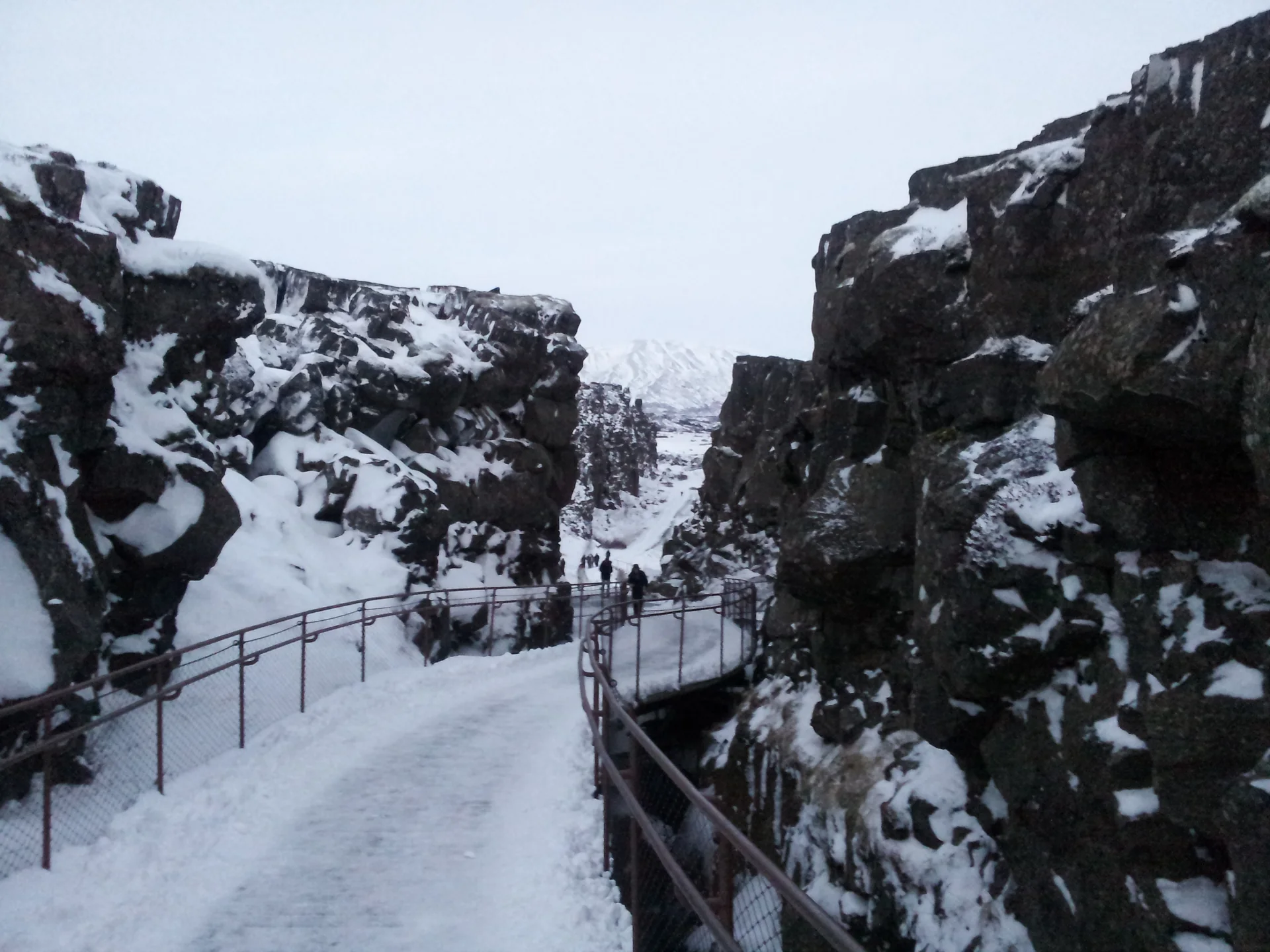 Vale de fenda no Parque Nacional Þingvellir, com paredões de rocha, vegetação baixa e céu aberto.