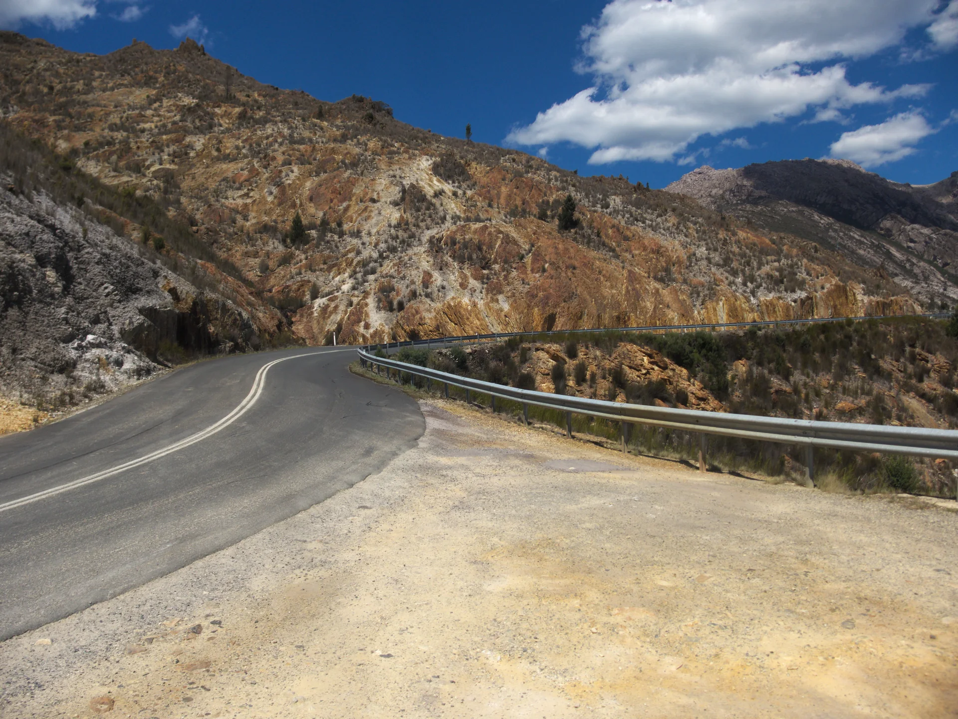 Trecho asfaltado da Lyell Highway com guarda-corpo, curva e encostas rochosas perto de Queenstown, na Tasmânia.