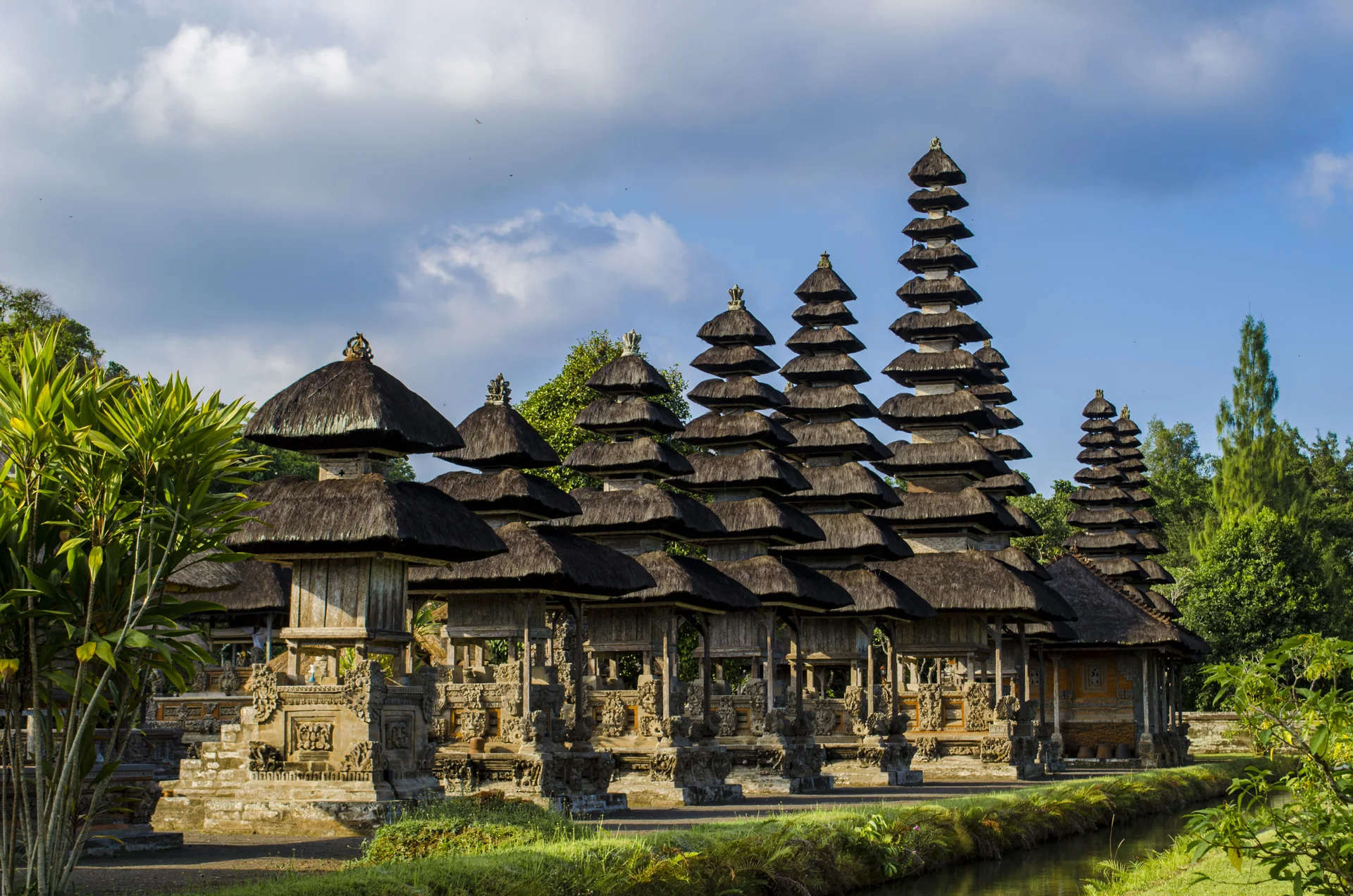 Pavilhões de telhado escalonado no Pura Taman Ayun, em Mengwi, vistos de uma área externa aberta e sem visitantes em primeiro plano.