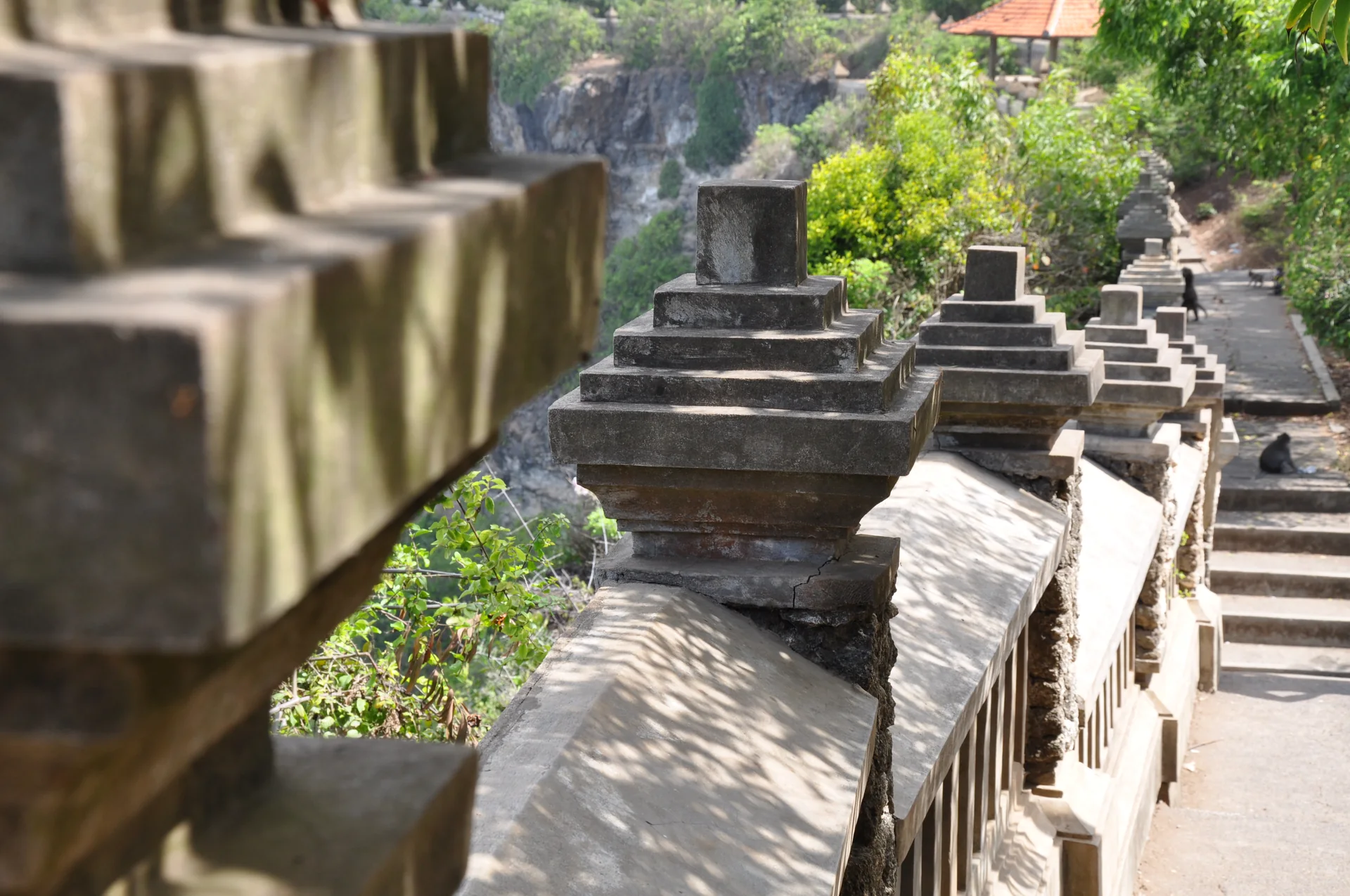 Percurso pavimentado e mureta de pedra no entorno de Pura Luhur Uluwatu, fotografados sem pessoas identificáveis.