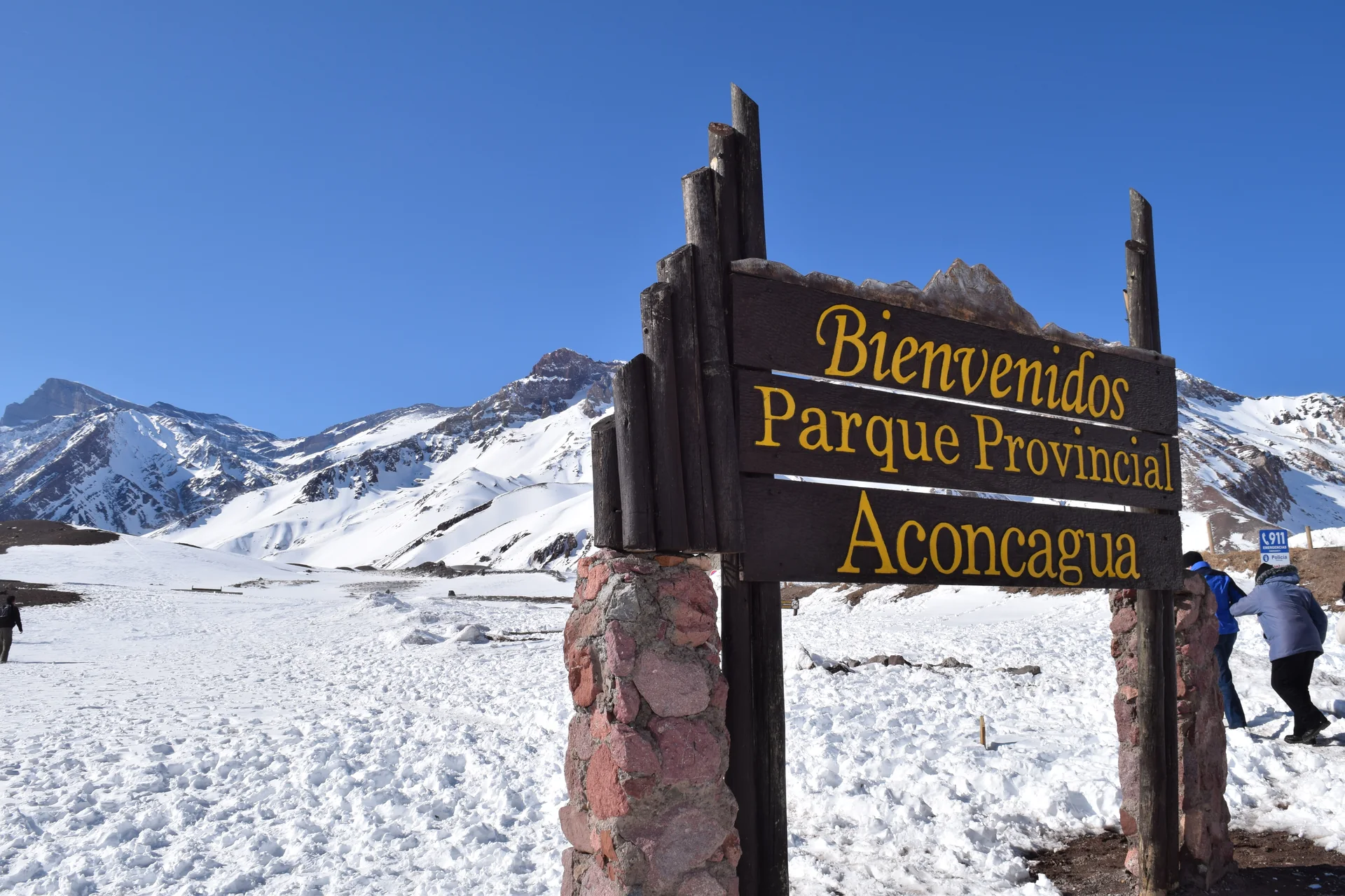 Placa de boas-vindas do Parque Provincial Aconcagua diante de montanhas com neve e céu azul.