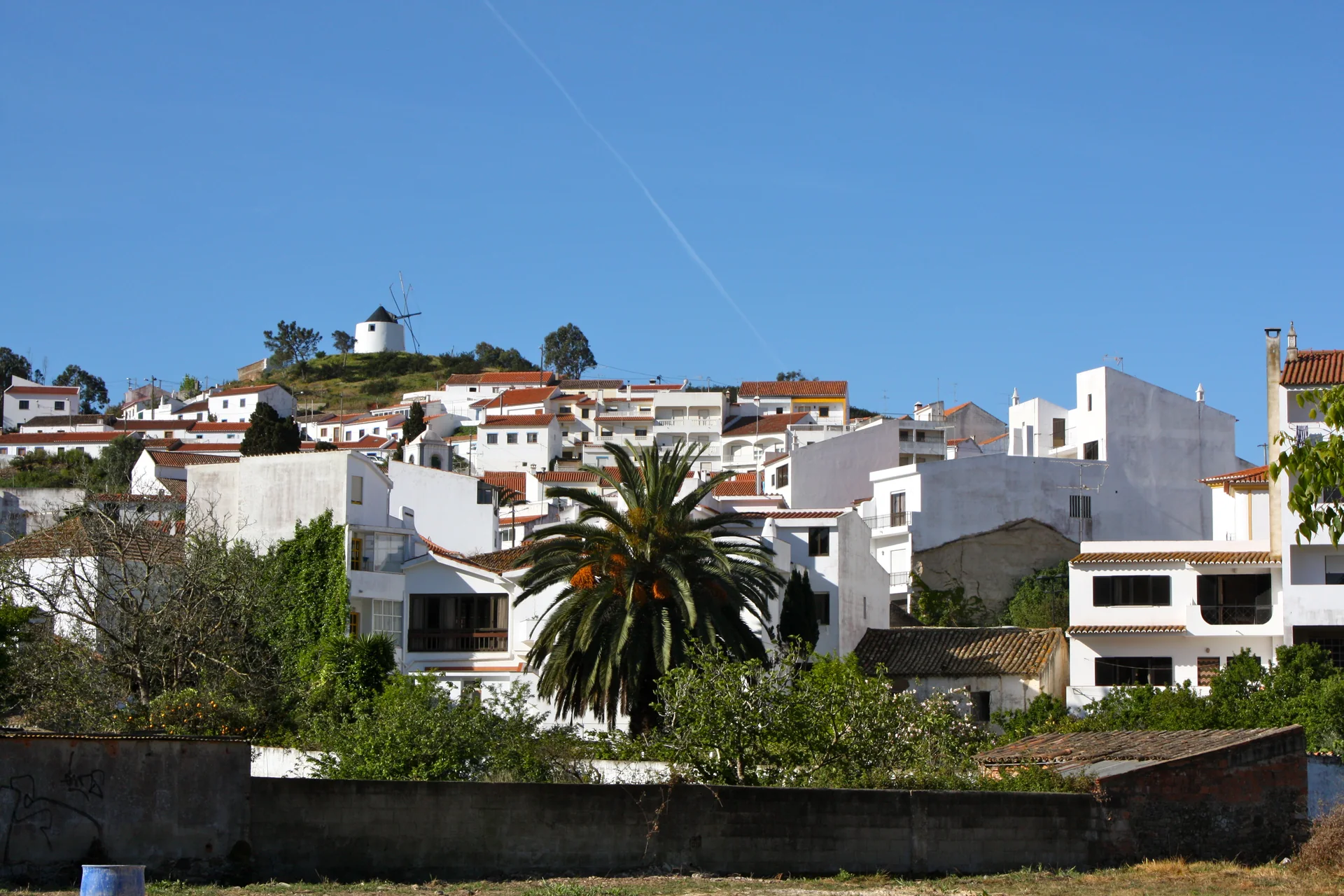 Casas e moinho em Odeceixe, no oeste do Algarve, entre vegetação e relevo baixo.