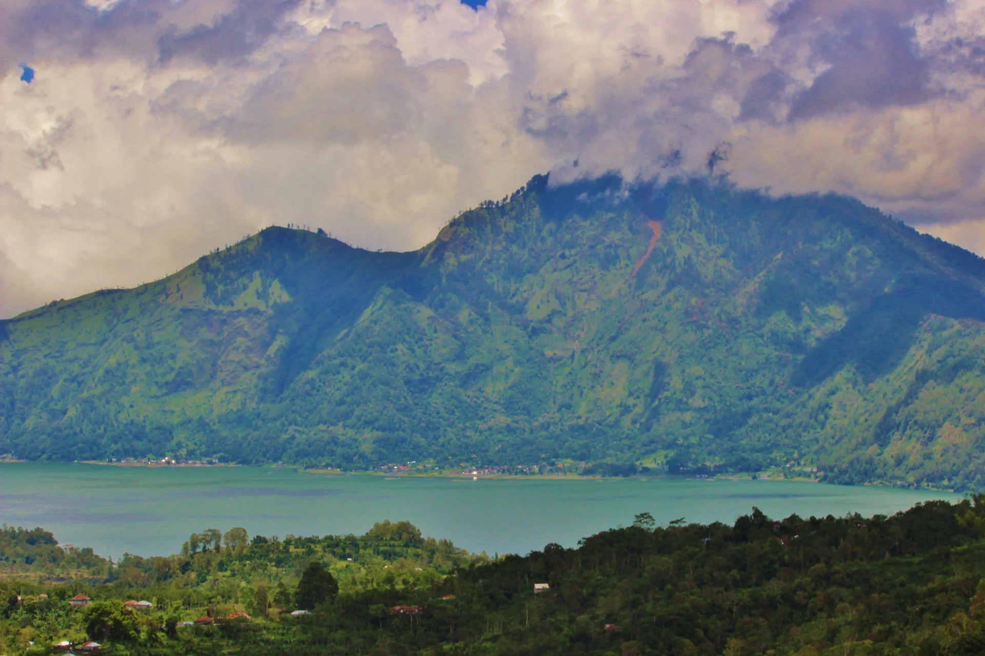 Lago Batur diante de encosta vulcânica verde e céu nublado na região de Kintamani.