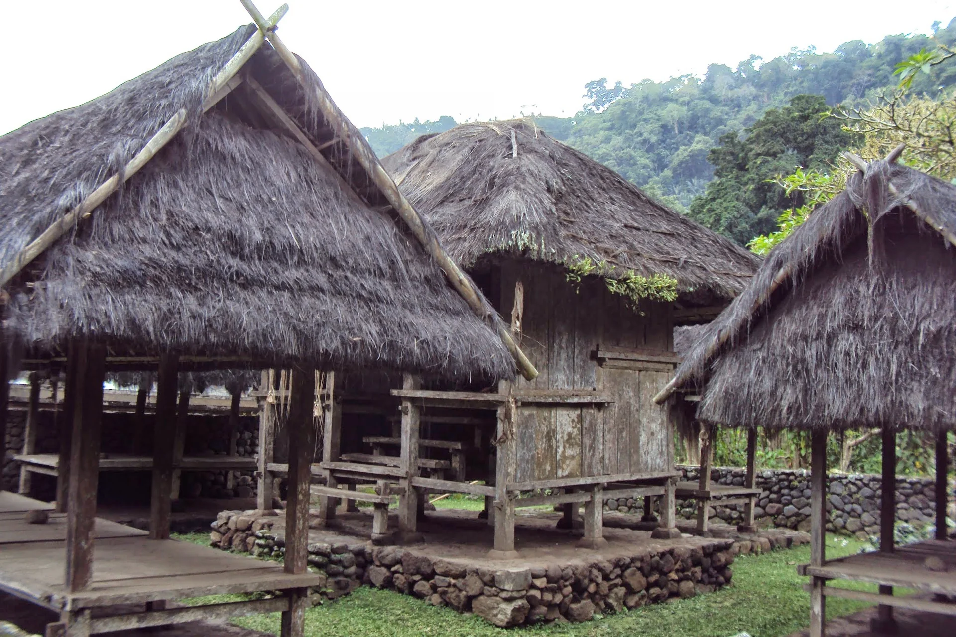 Construções de madeira com telhados de palha da arquitetura Bali Aga em Tenganan, diante de vegetação de encosta.