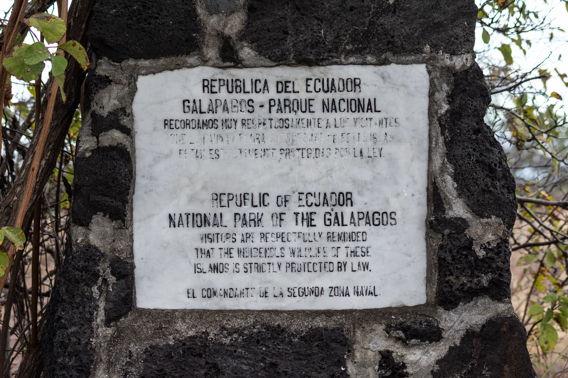 Placa bilíngue em uma estrutura de pedra, fotografada em área protegida de Galápagos.
