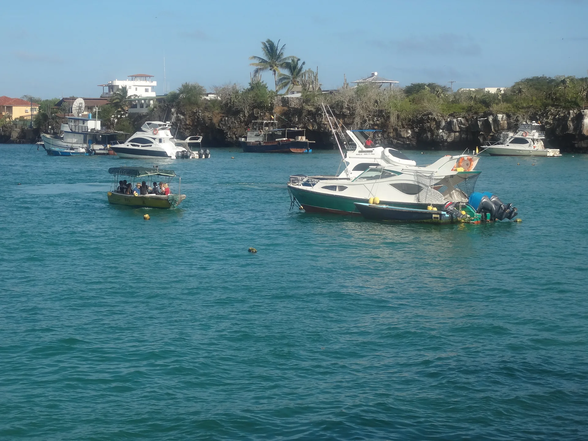Embarcações de pequeno porte na água junto à orla de Puerto Ayora, vistas de longe.