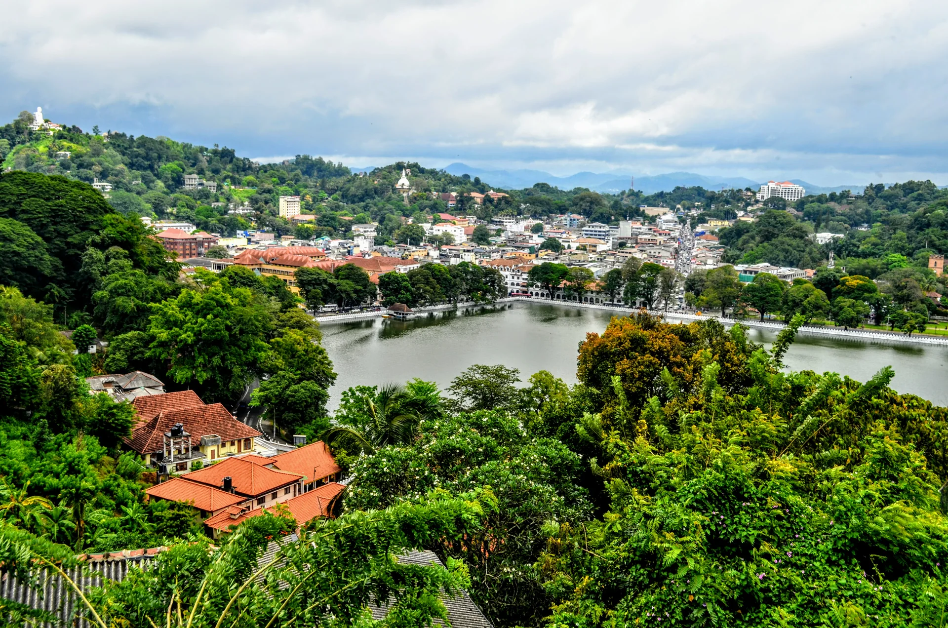 Panorama de áreas urbanas de Kandy entre árvores e encostas montanhosas.