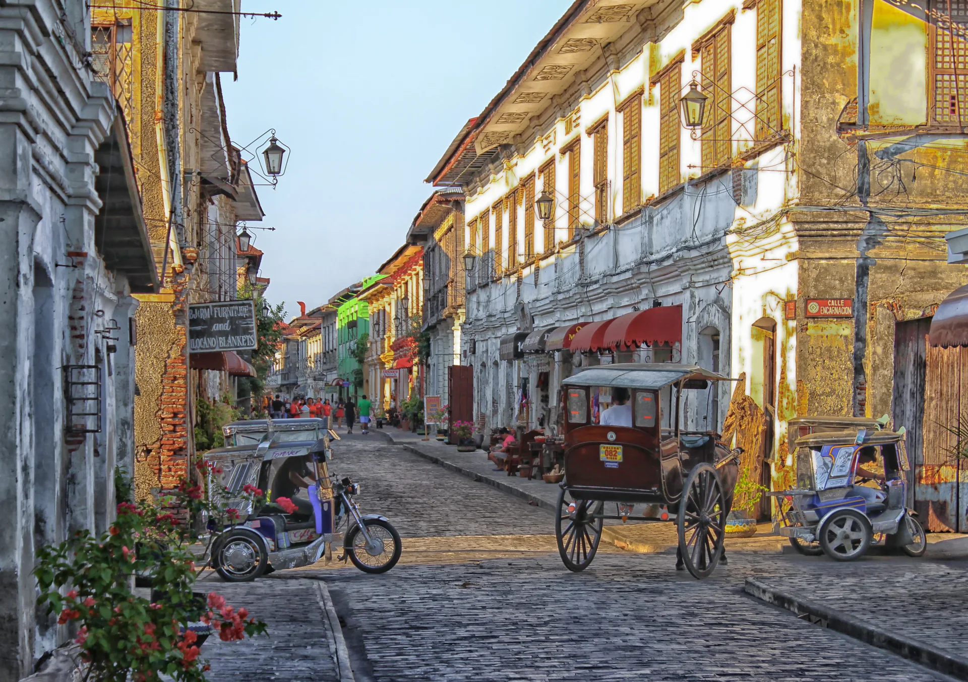 Rua histórica de Vigan com pavimento de pedra, fachadas antigas, pedestres e veículos locais nas Filipinas.