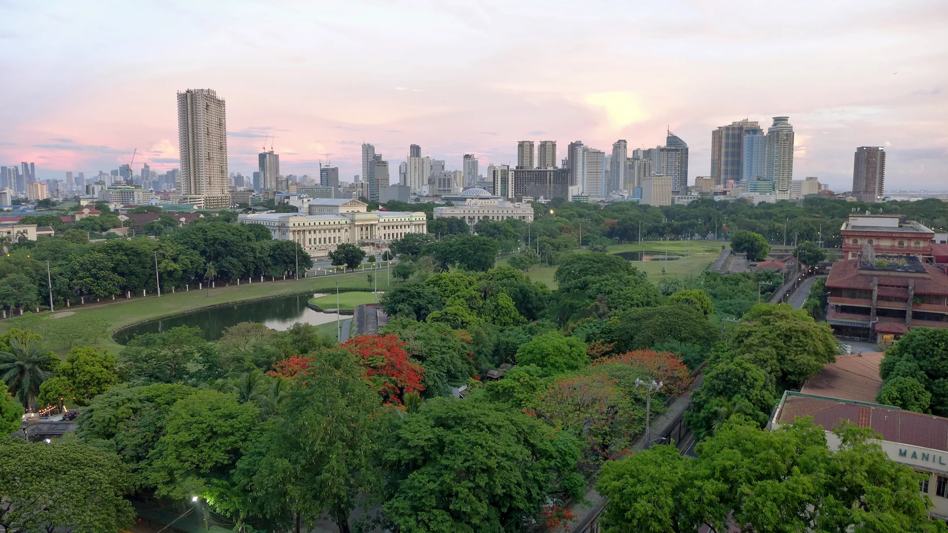 Parque arborizado e conjunto de edifícios no panorama de Manila ao entardecer, vistos a partir de Intramuros.