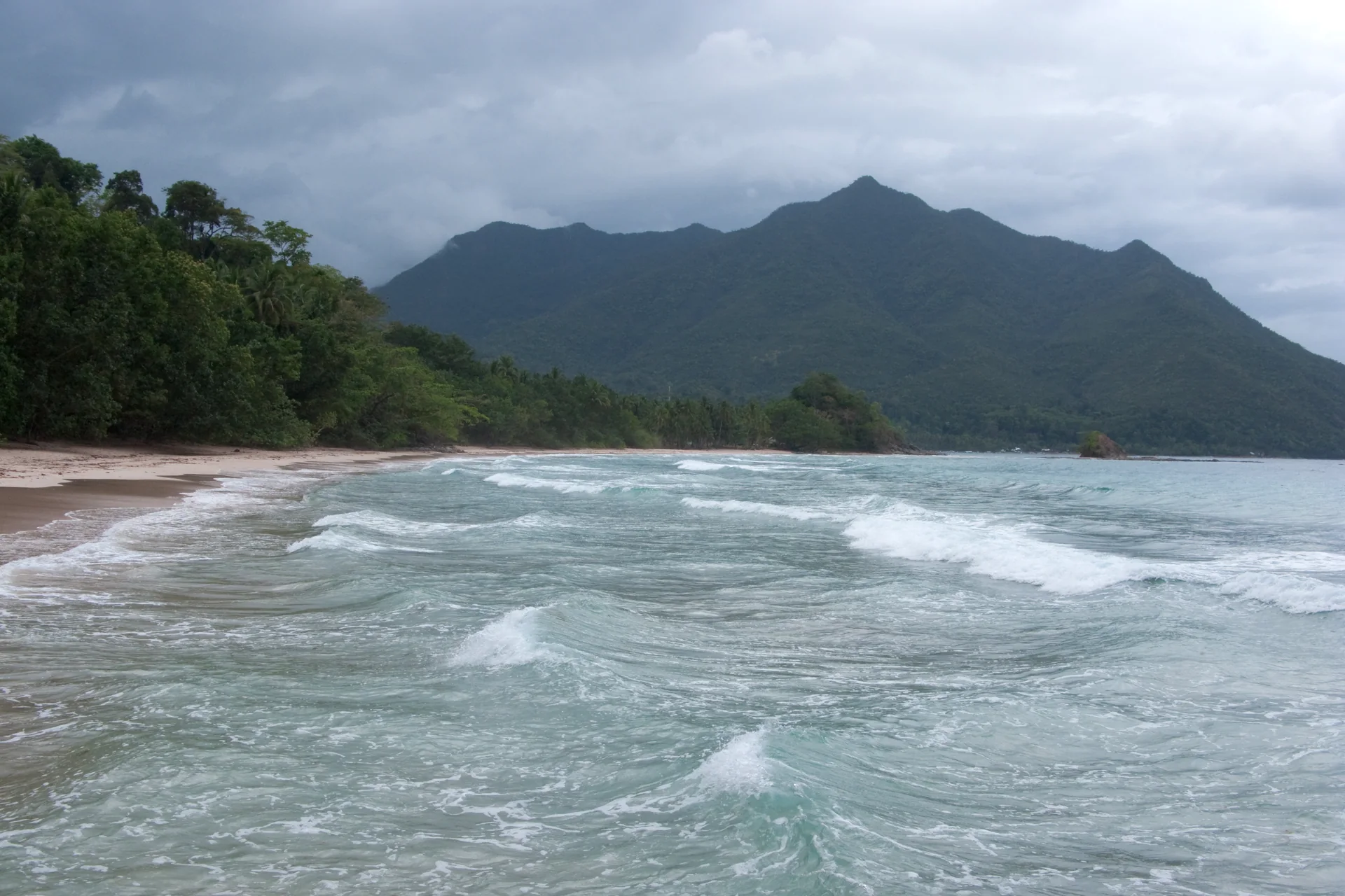 Praia de Sabang diante de montanhas calcárias e mar agitado sob céu encoberto, em Palawan, Filipinas.