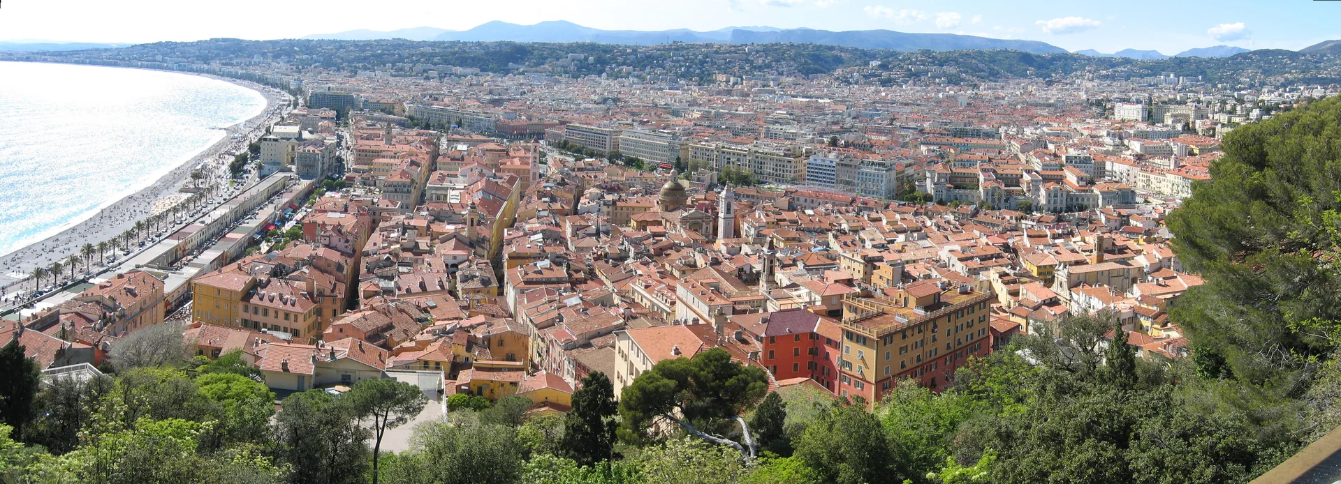 Vista panorâmica de Vieux Nice a partir da Colline du Château, com telhados, frente marítima e colinas ao fundo.