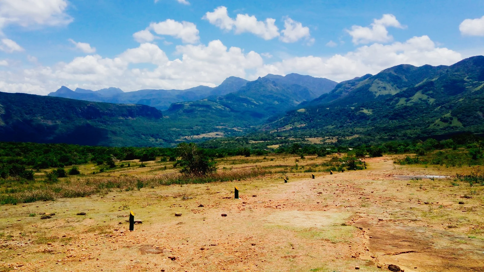 Campo aberto de gramíneas e solo claro diante de uma cadeia de montanhas em Pitawala Pathana, Matale.