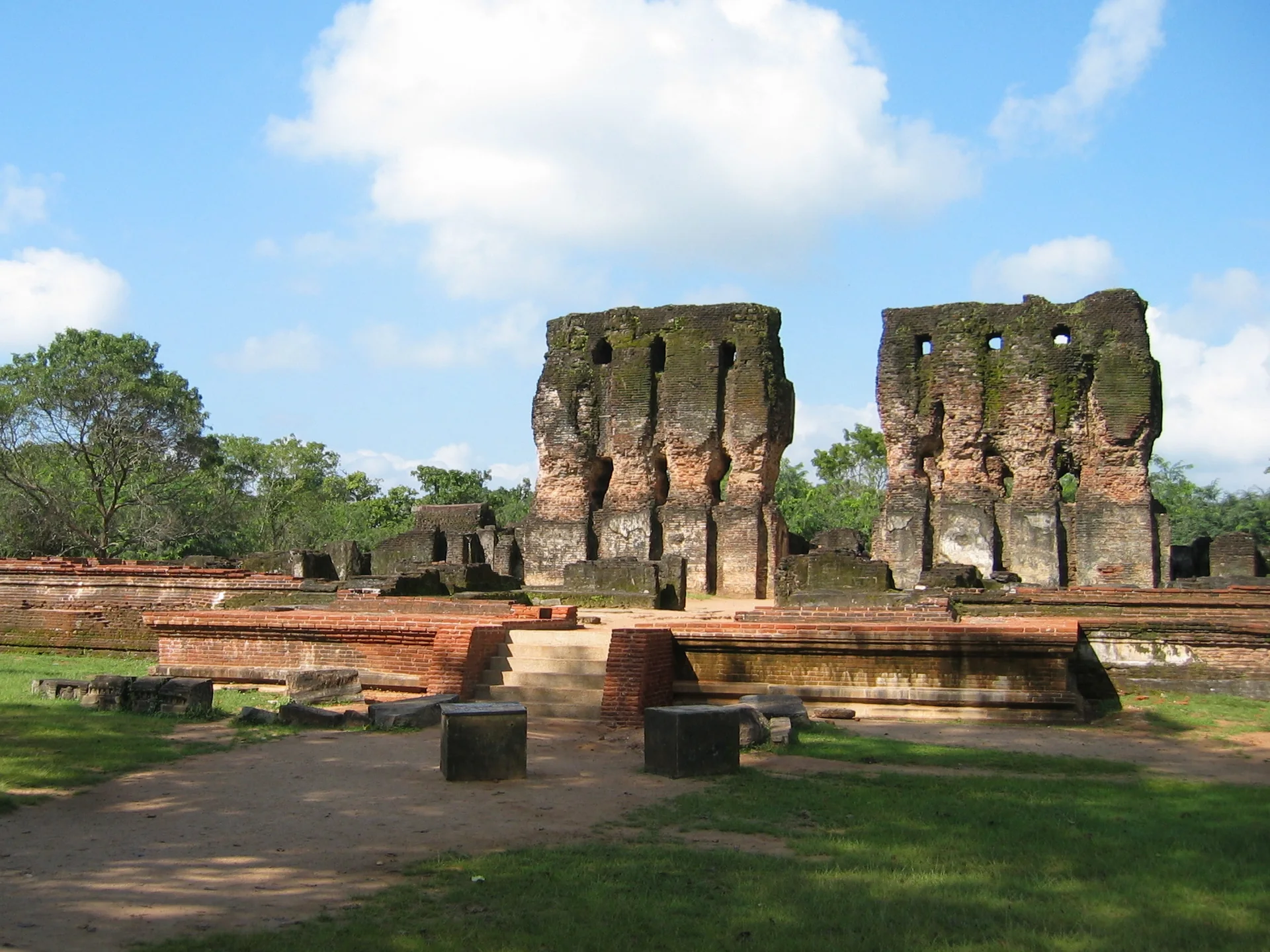 Paredes de tijolo e estruturas remanescentes do Palácio Real de Polonnaruwa em meio a gramado e árvores.