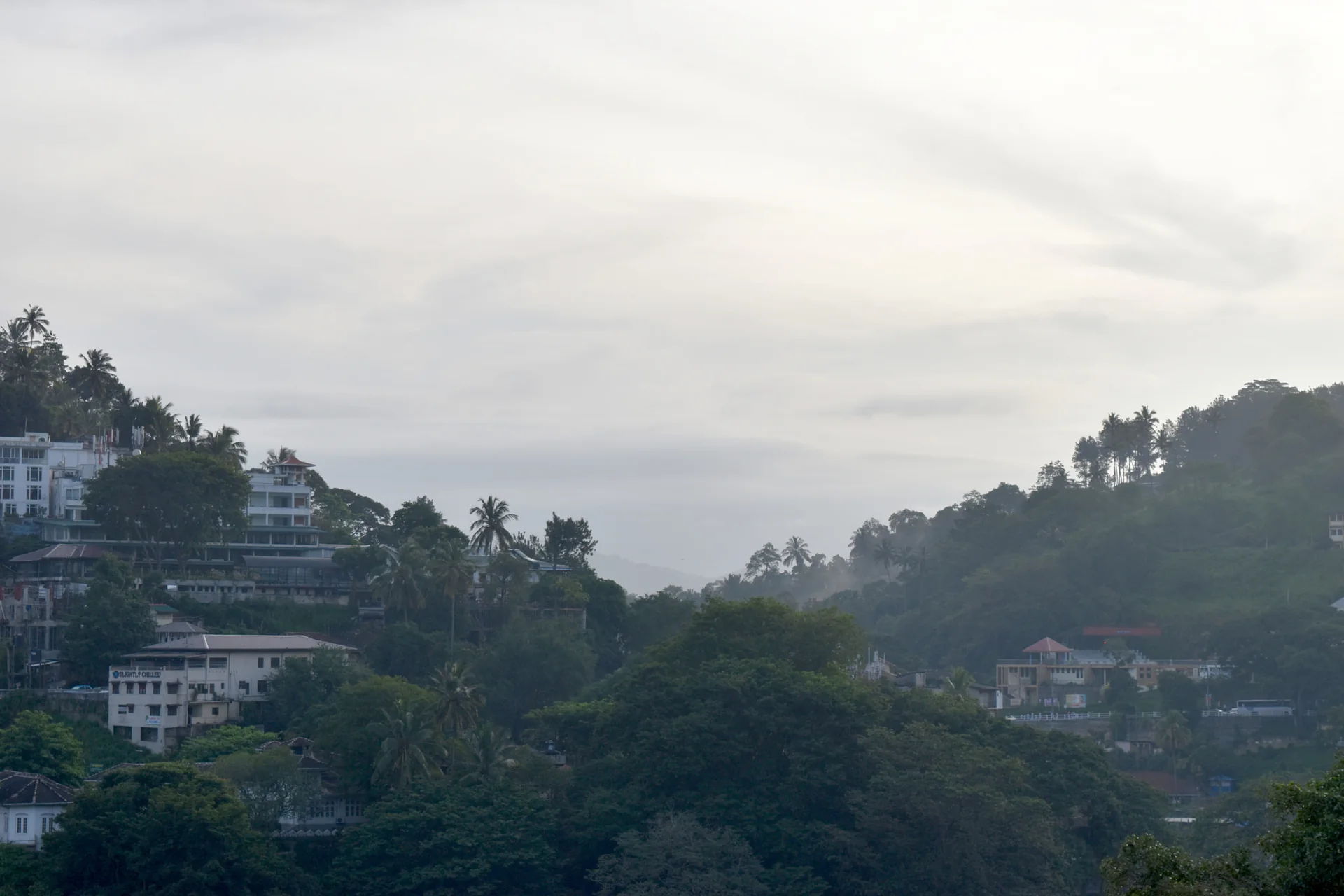 Casas entre encostas arborizadas de Kandy, sob luz matinal e céu parcialmente encoberto.