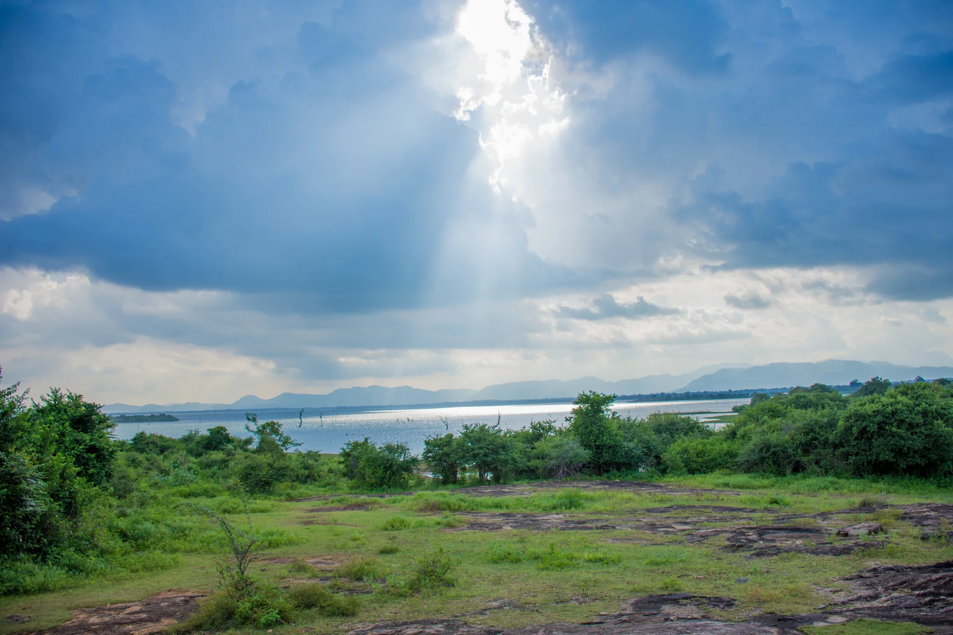 Lago, vegetação baixa e céu com raios de sol no Parque Nacional Udawalawe, Sri Lanka.