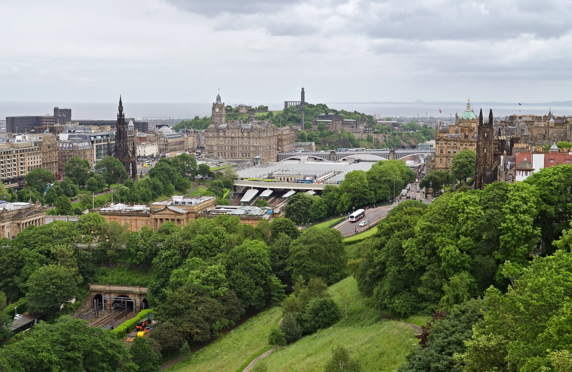 Vista elevada do vale de Waverley, da estação Edinburgh Waverley e de North Bridge, com jardins e o relevo urbano de Edimburgo.