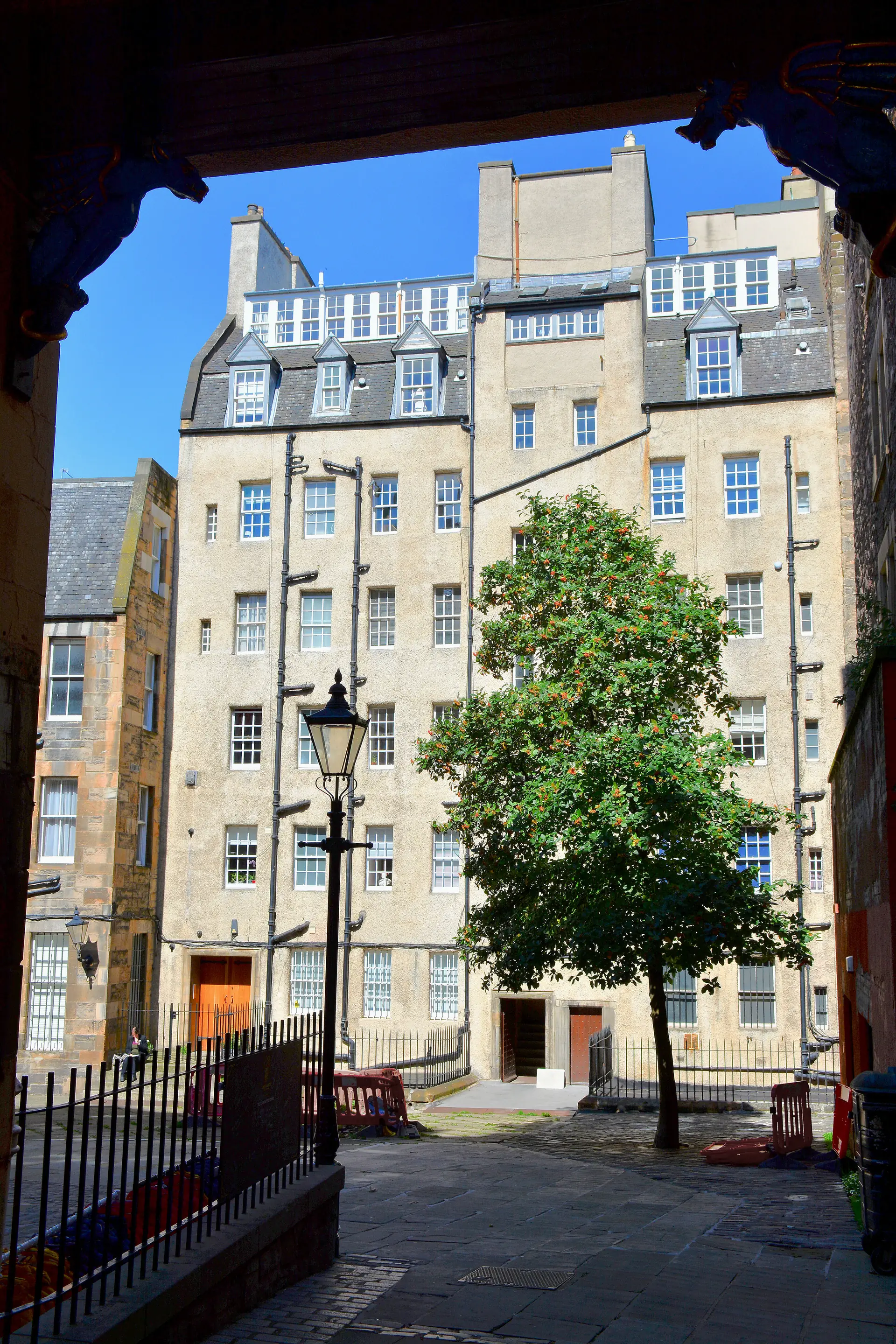 Fachada residencial clara de Blackie House vista a partir de Makars' Court, com árvore, luminária e passagem de pedra na Old Town de Edimburgo.