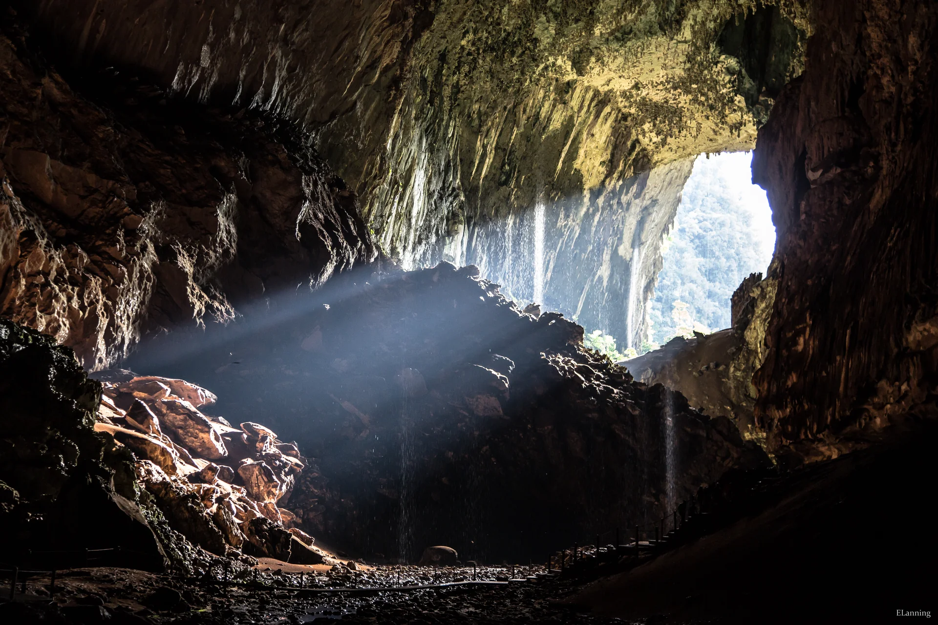 Interior de caverna no Parque Nacional Gunung Mulu, com entrada iluminada e formações rochosas.