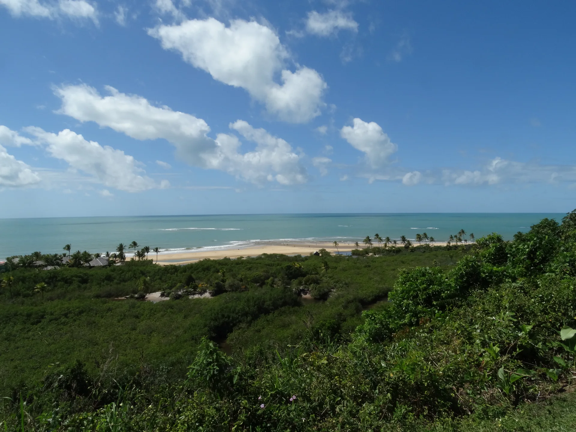 Vista ampla da Praia dos Nativos com faixa de areia, mar e vegetação em Trancoso.