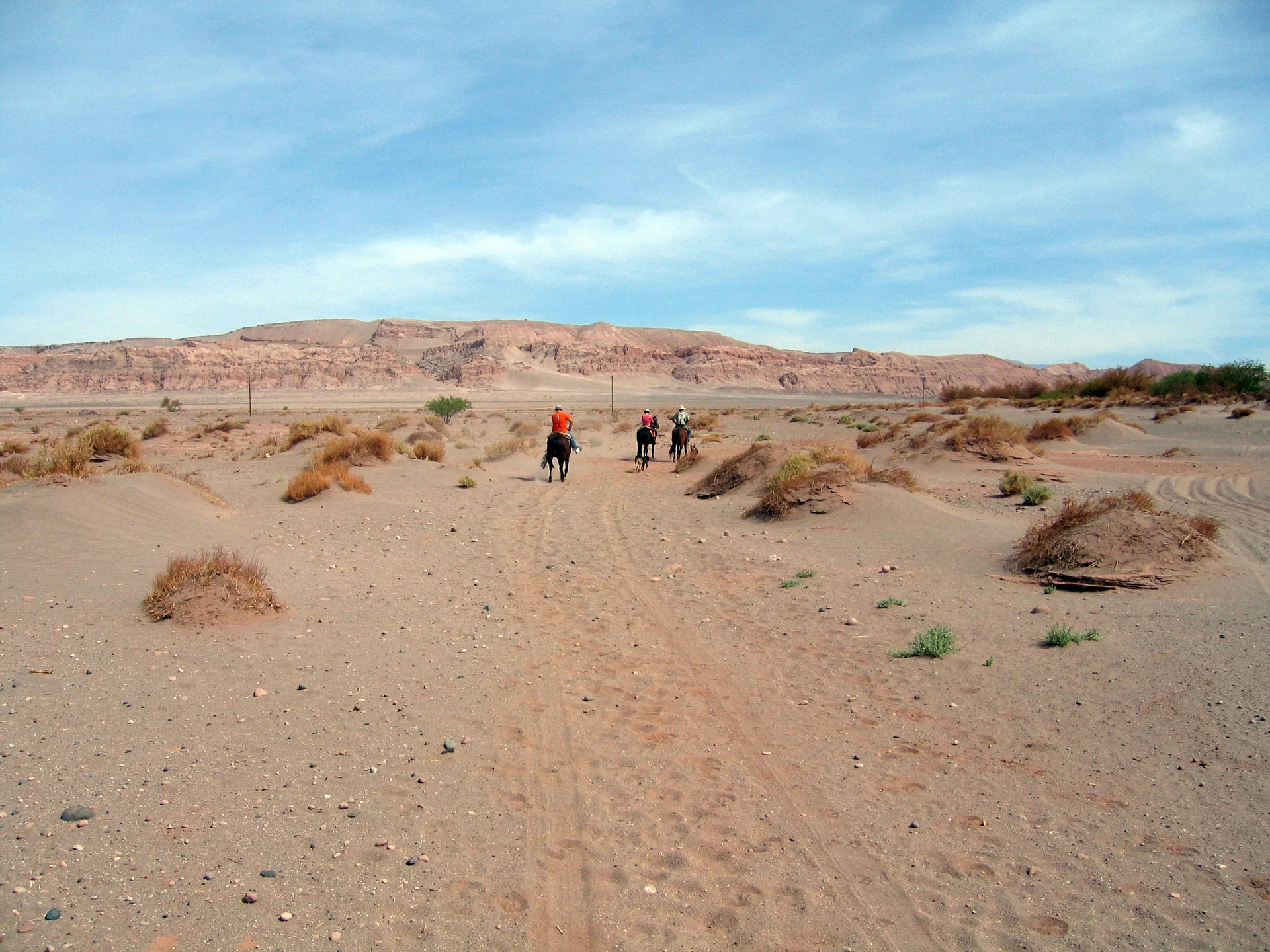 Vista diurna de San Pedro de Atacama, com construções de adobe, paisagem desértica e montanhas sob céu azul.