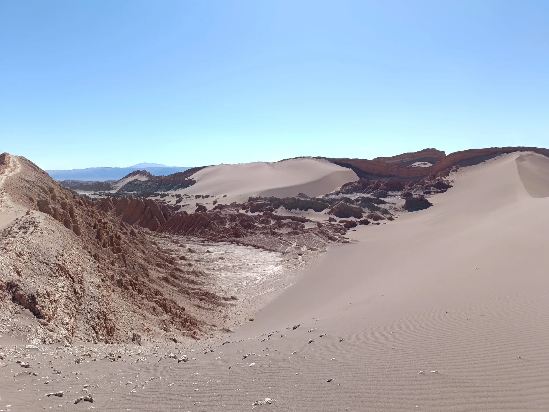 Dunas claras e formações rochosas do Valle de la Luna, no deserto de Atacama, sob céu azul limpo.