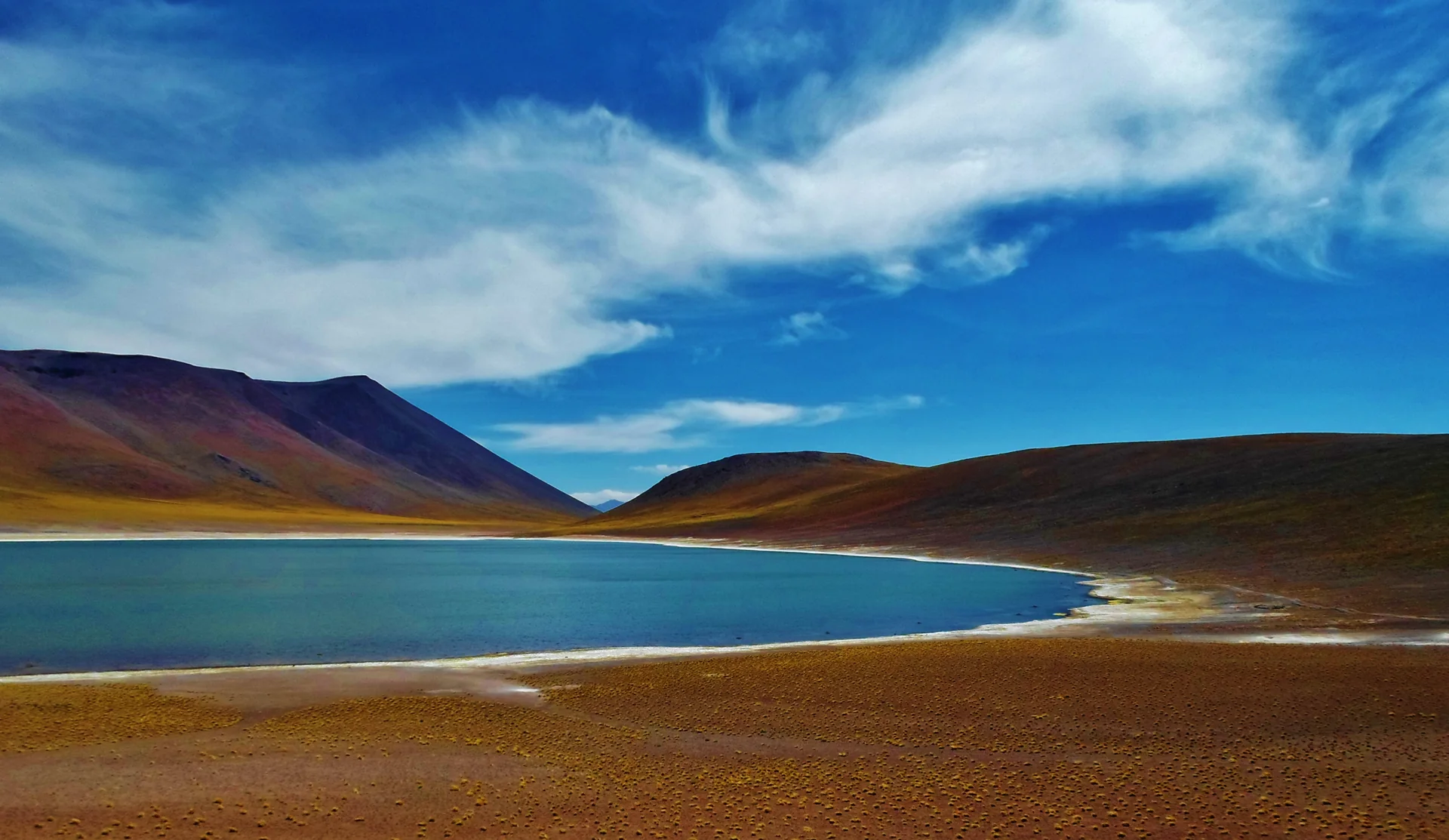 Lagoa azul entre montanhas no altiplano de Atacama, sob céu claro.
