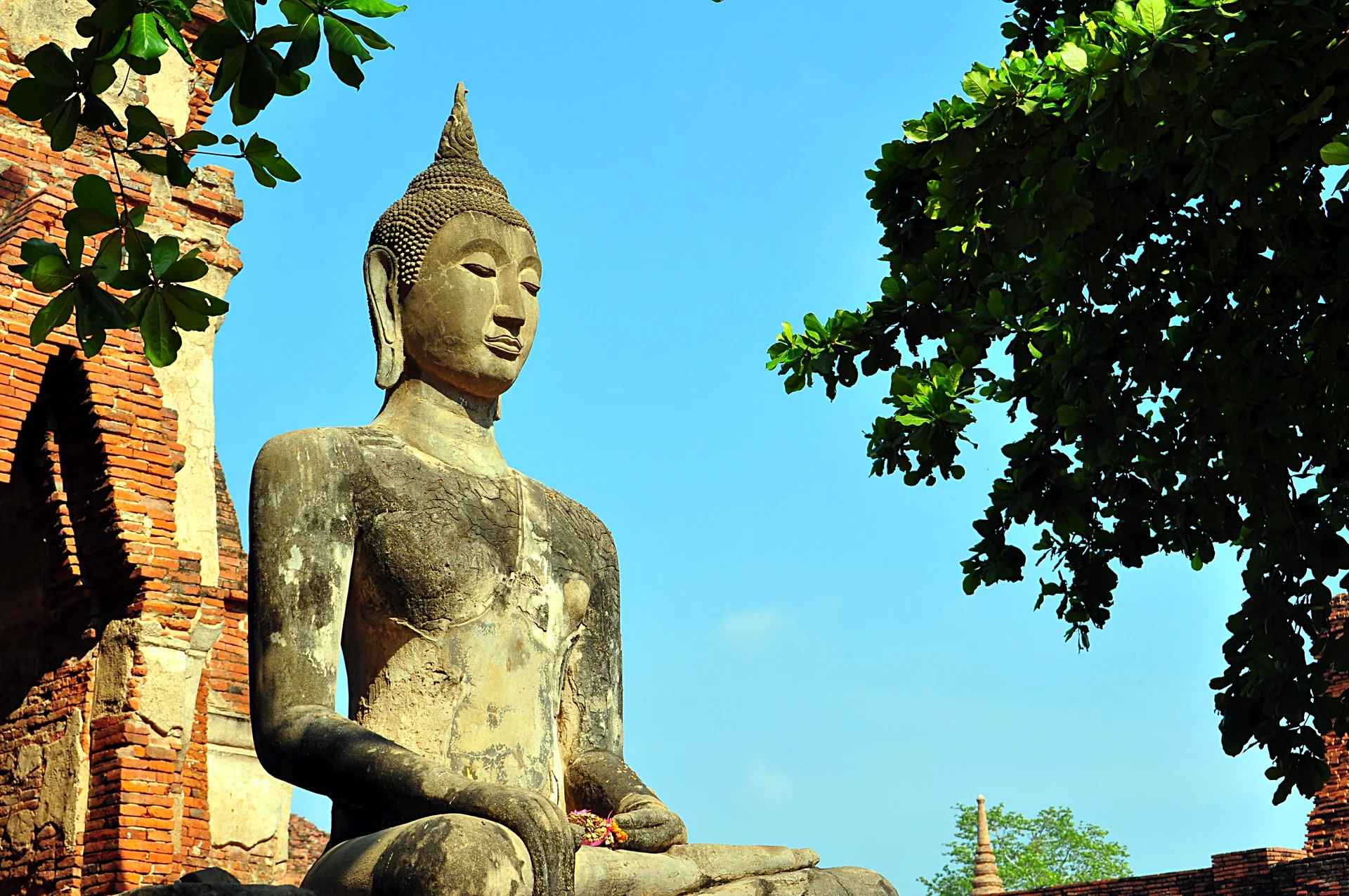 Imagem de Buda entre ruínas de tijolo em Wat Mahathat, Ayutthaya, sob céu azul.