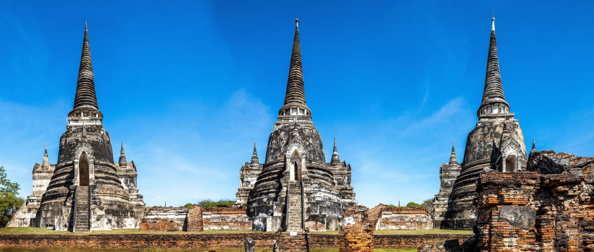 Panorama das três chedis de Wat Phra Si Sanphet, em Ayutthaya, sob céu azul.