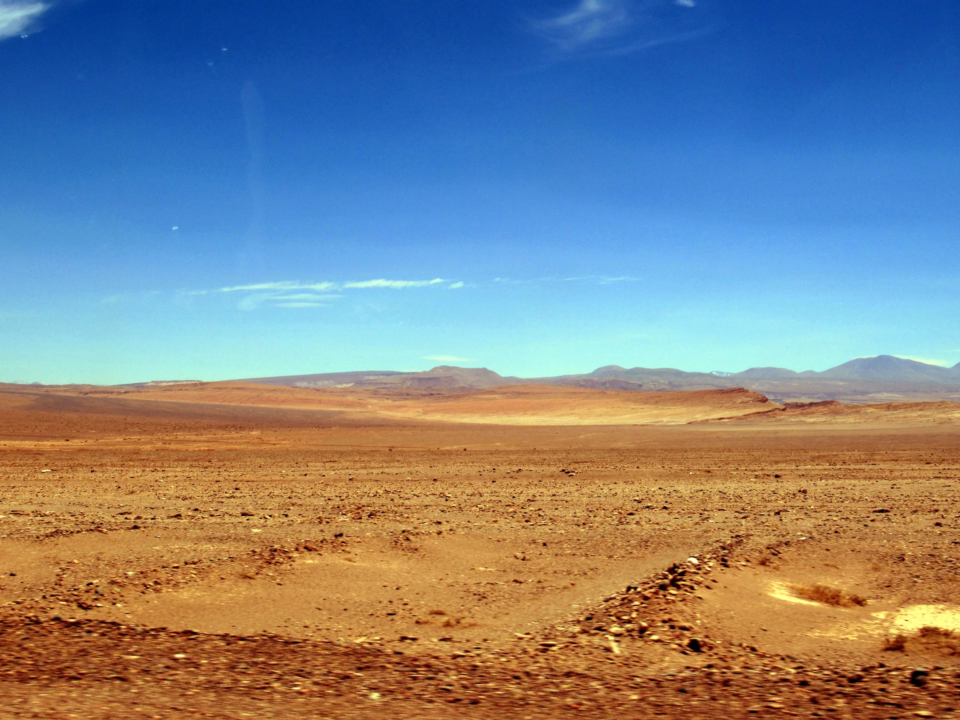 Paisagem árida do Llano de la Paciencia na Rota 23-CH, com montanhas ao fundo e céu azul.