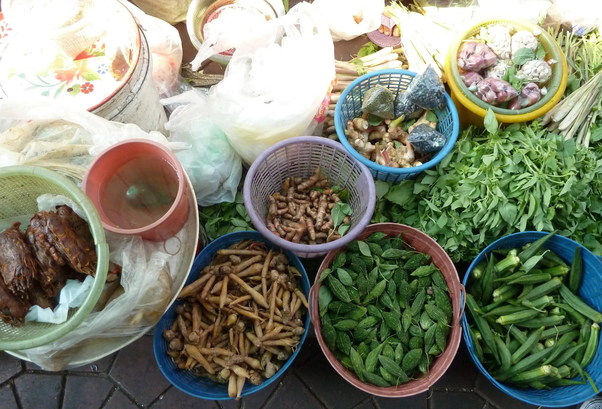 Ingredientes frescos, ervas e pimentas organizados em recipientes em uma banca de mercado de Bangkok.