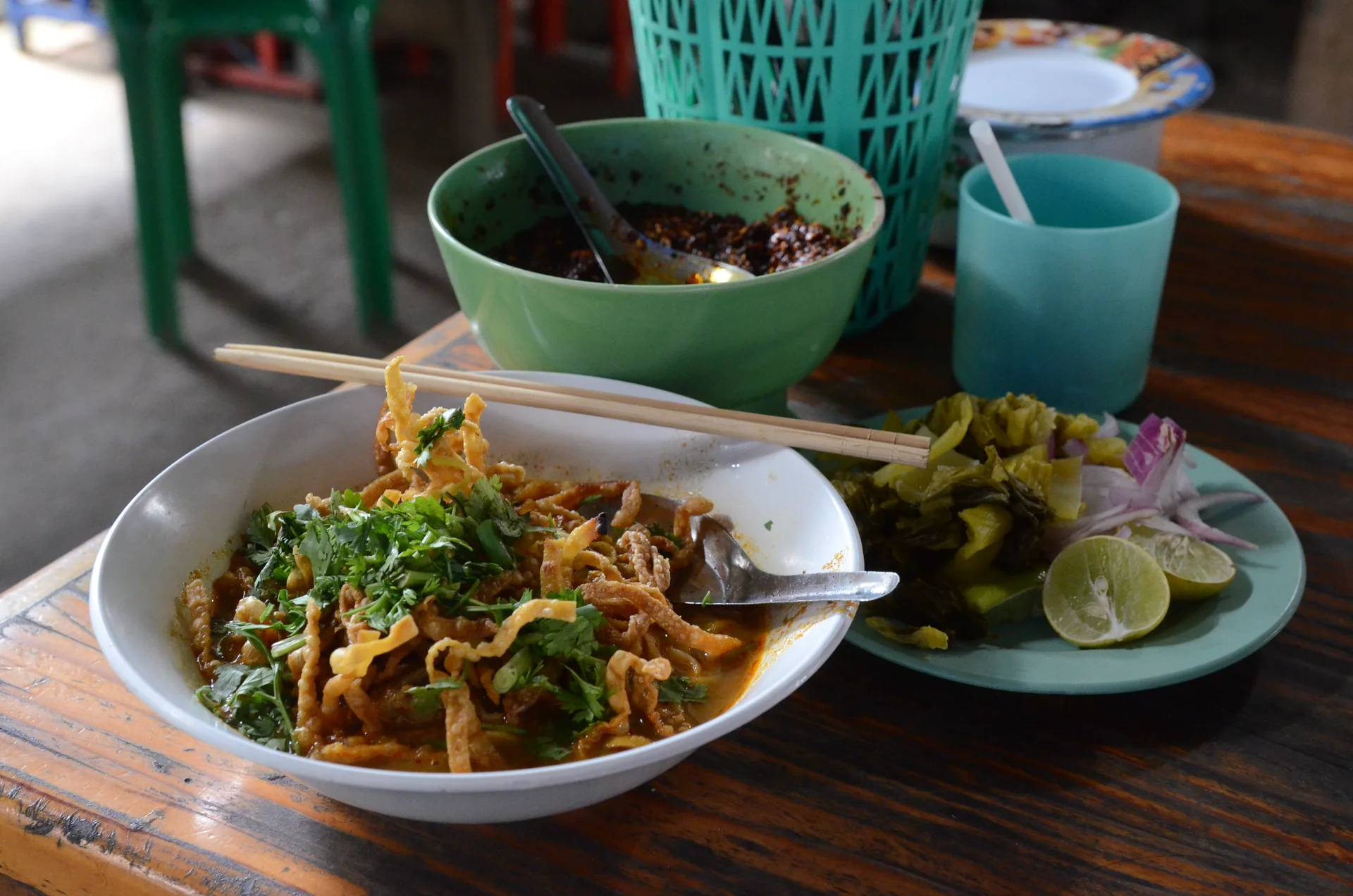 Tigela de khao soi com macarrão, caldo de curry, macarrão crocante e acompanhamentos.