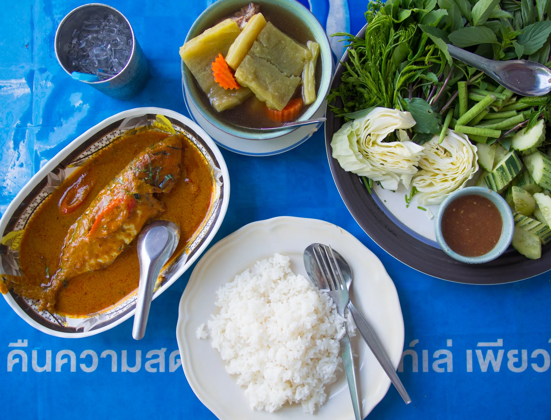 Refeição com curry de peixe, sopa, arroz e legumes em uma mesa.
