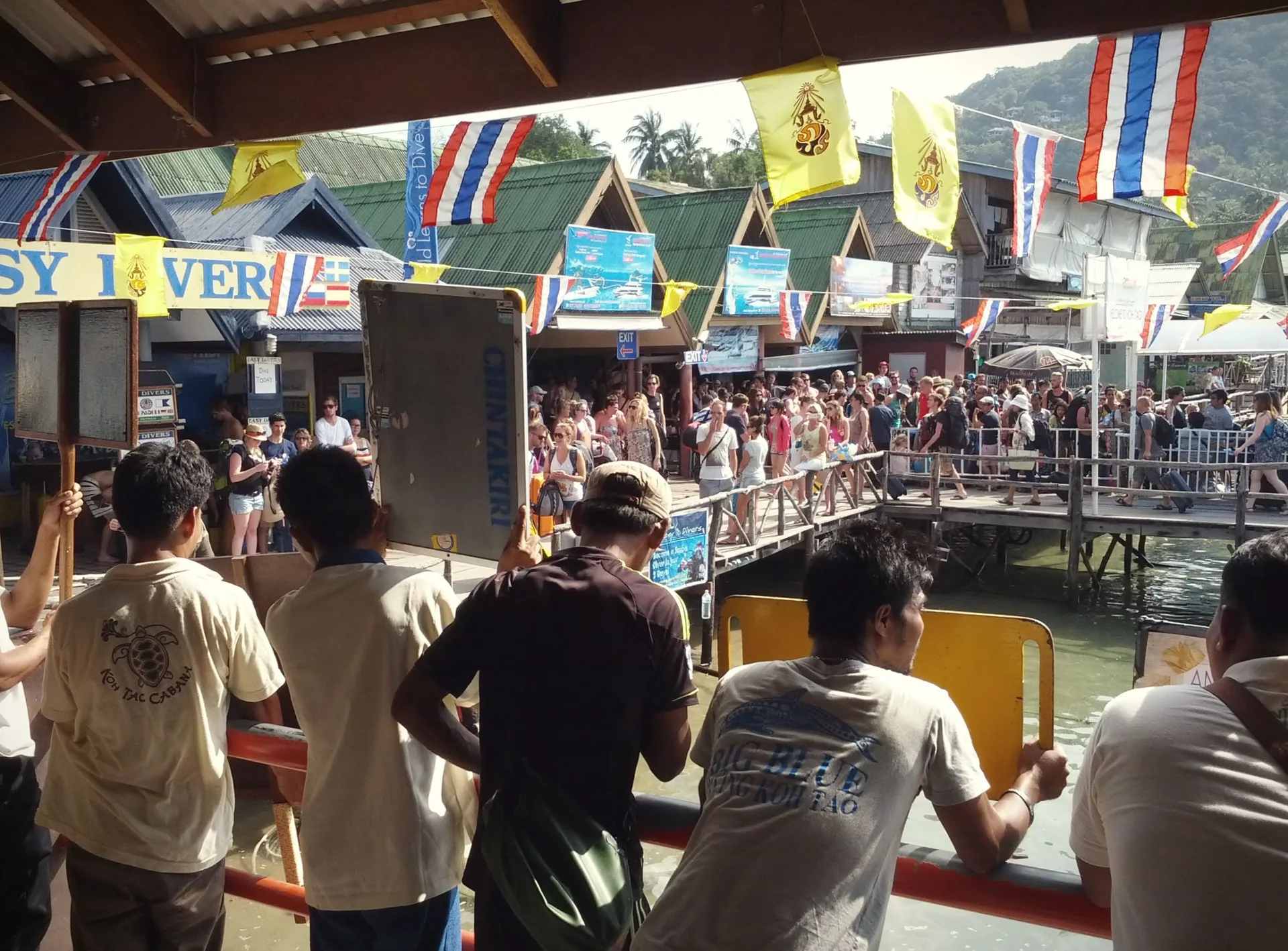 Viajantes vistos em um píer de chegada em Koh Tao, junto a uma embarcação durante o dia.