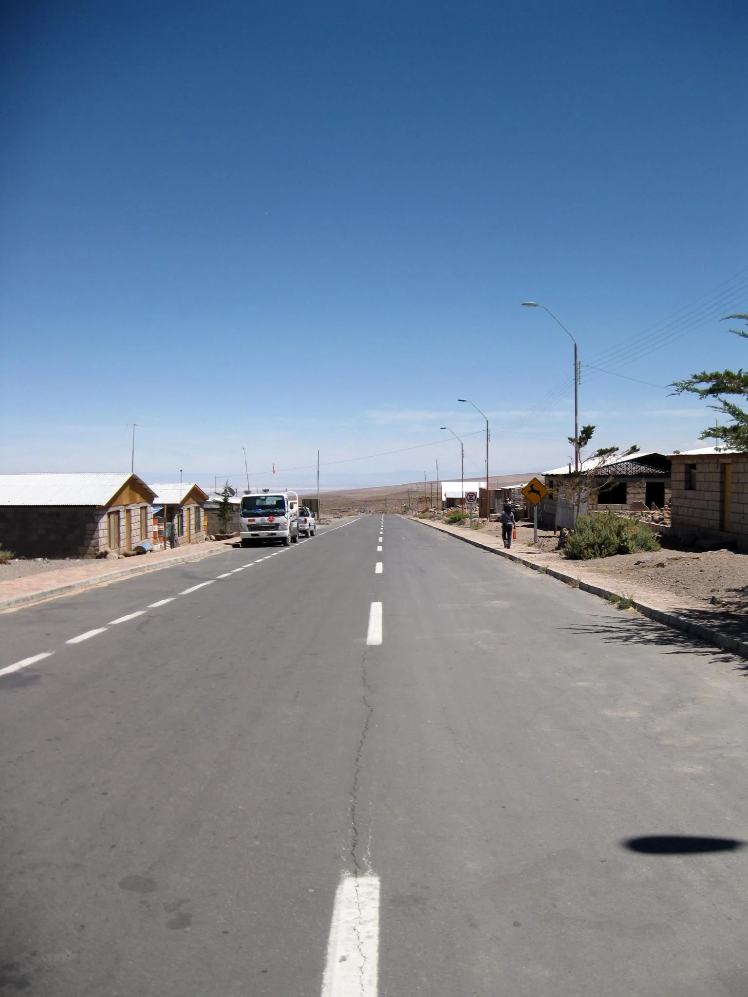 Rua asfaltada no centro de Socaire, com casas baixas e montanhas ao fundo em dia claro.