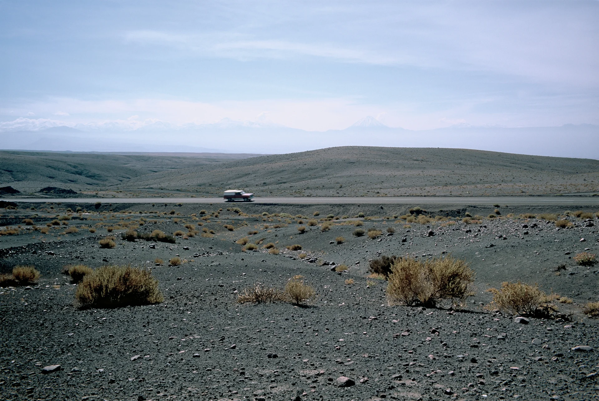 Estrada atravessando uma paisagem árida nos arredores de San Pedro de Atacama, com o Licancabur pouco visível ao fundo sob névoa.