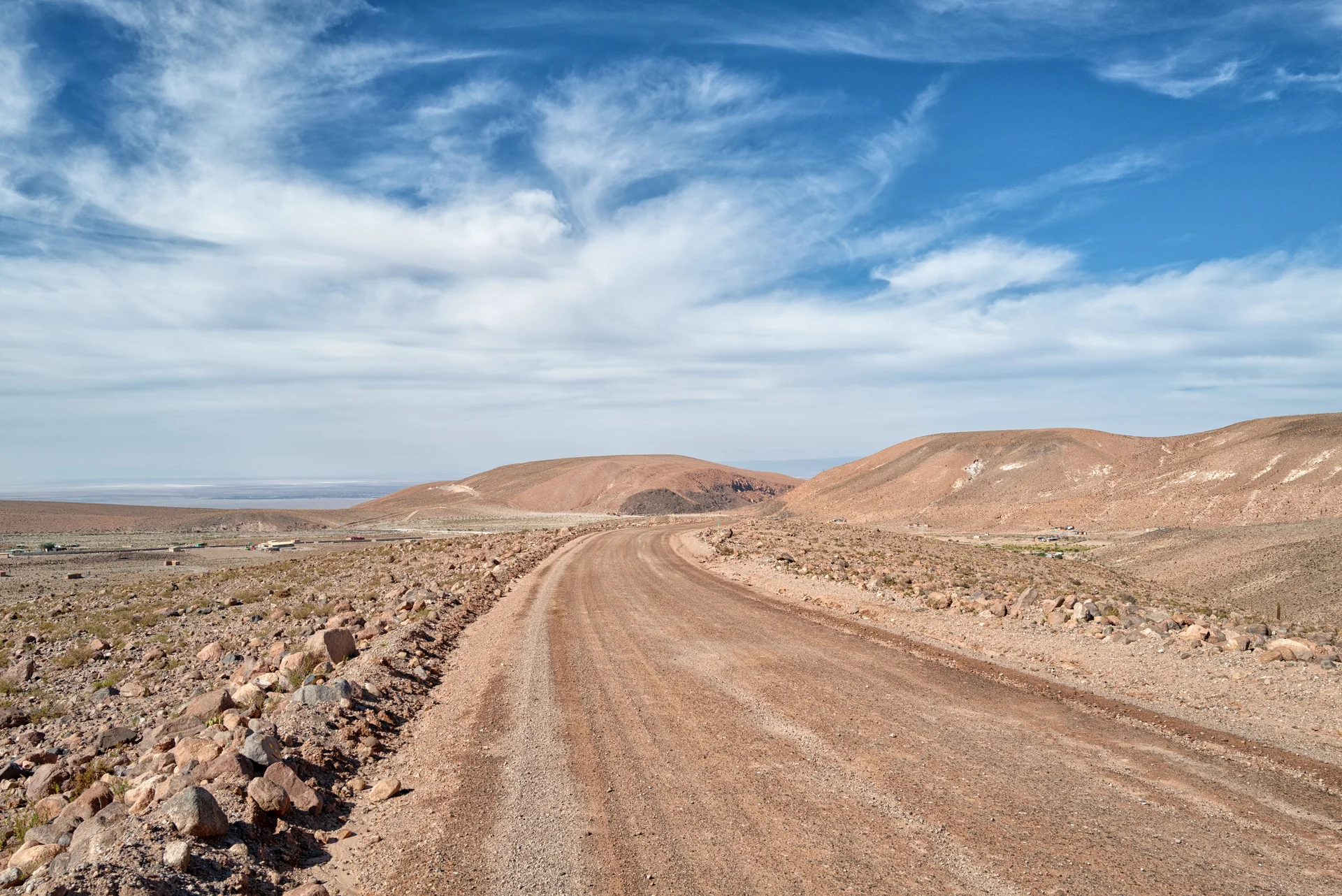 Estrada de terra no deserto do Atacama, entre colinas áridas e céu parcialmente azul, nas proximidades de Puritama.