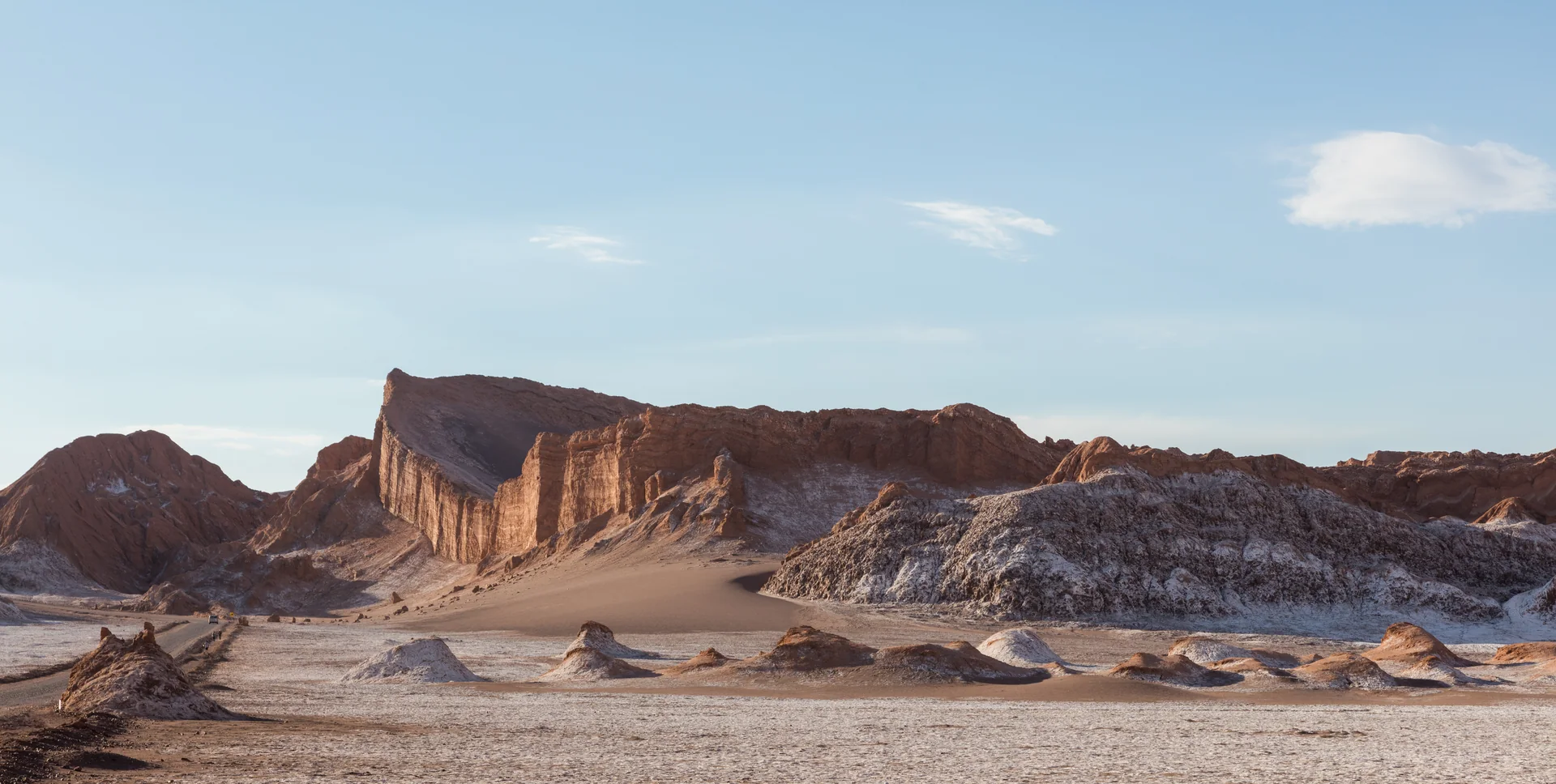 Formação rochosa do Anfiteatro no Valle de la Luna, cercada por solo claro e montanhas áridas sob céu azul.
