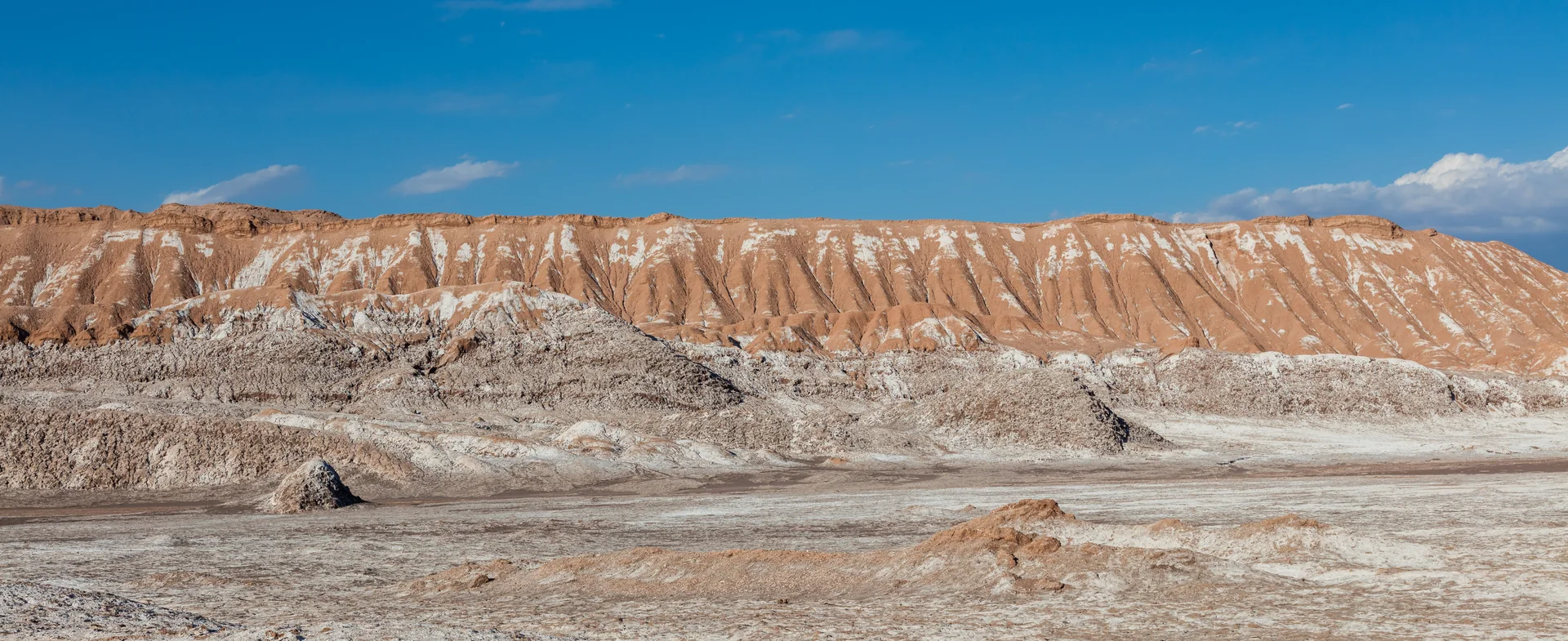Faixa de paredões estratificados com sal aparente no Valle de la Luna, sob céu azul claro.