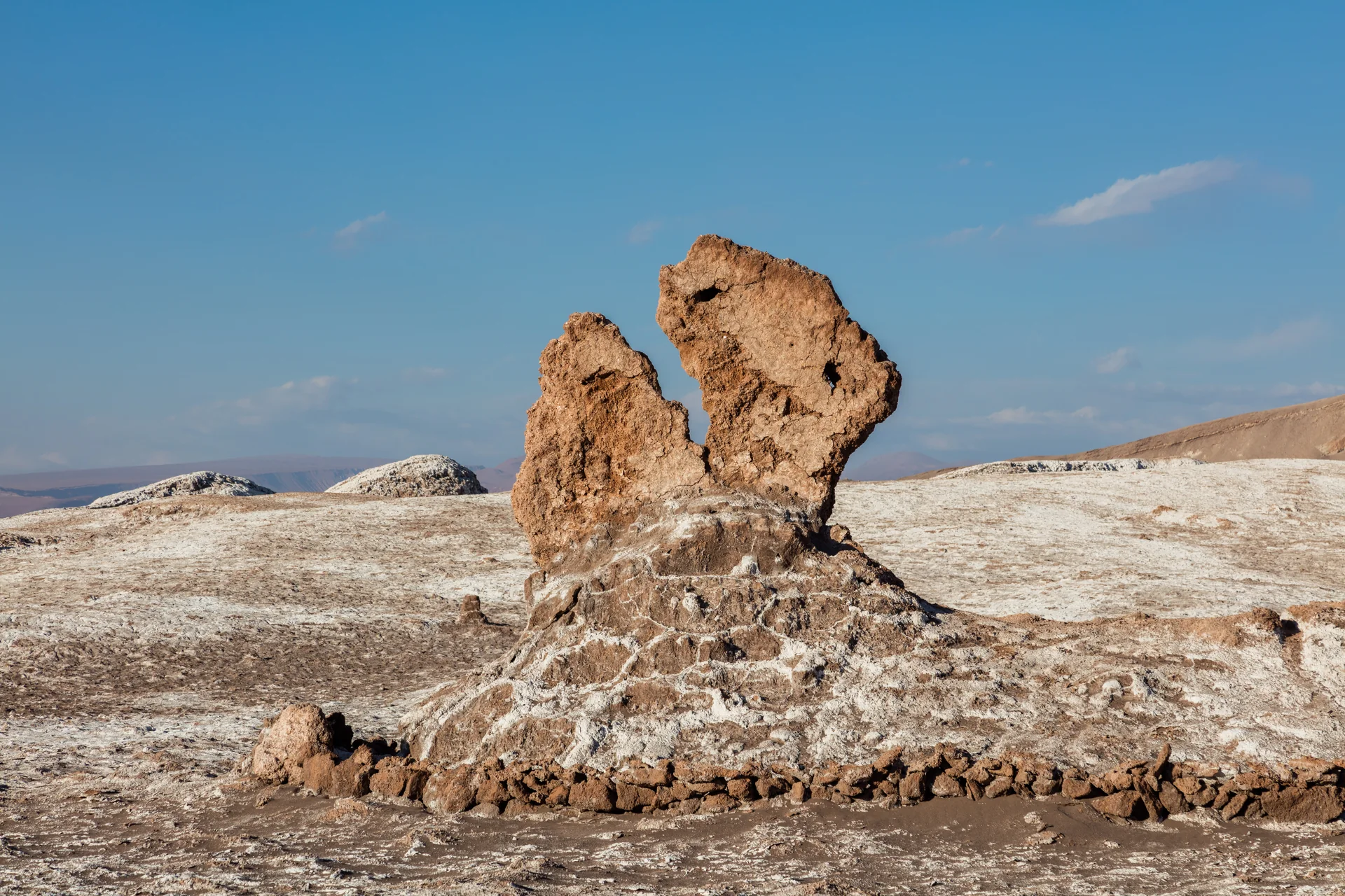 Formação de Las Tres Marías sobre crosta clara de sal no Valle de la Luna, sob céu azul.