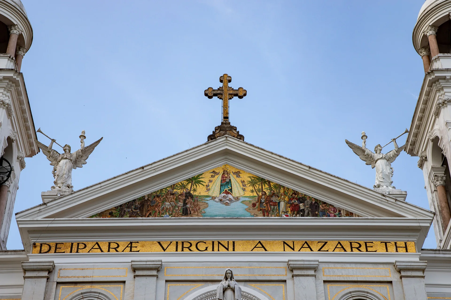 Frontão da Basílica Santuário de Nazaré em Belém, com mosaico, anjos e cruz sob céu azul.