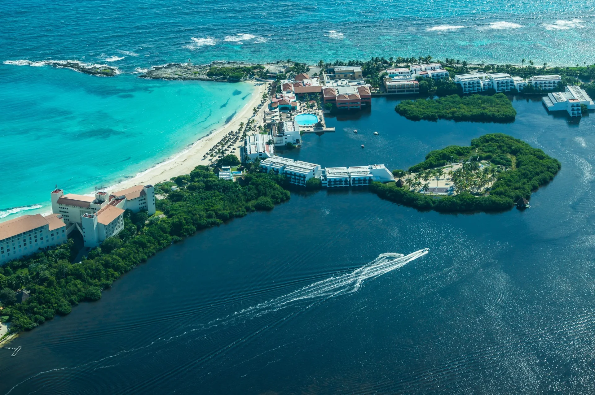 Vista aérea diurna de um trecho de Cancún, com praia, mar do Caribe, Lagoa Nichupté e vegetação costeira.